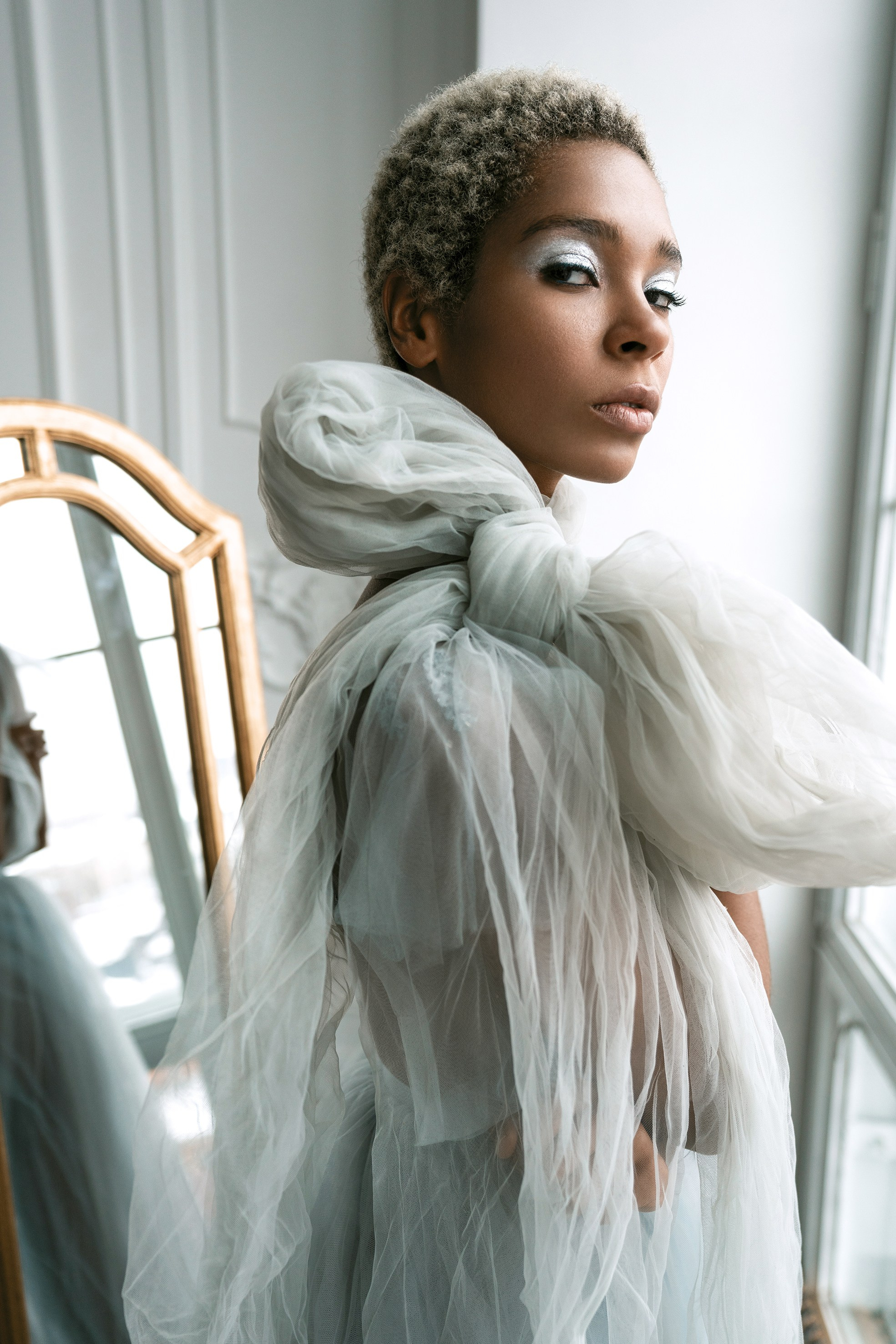 Frau mit silbernem Make-up blickt in einem Hochzeitsoutfit mit großer Schleife direkt in die Kamera