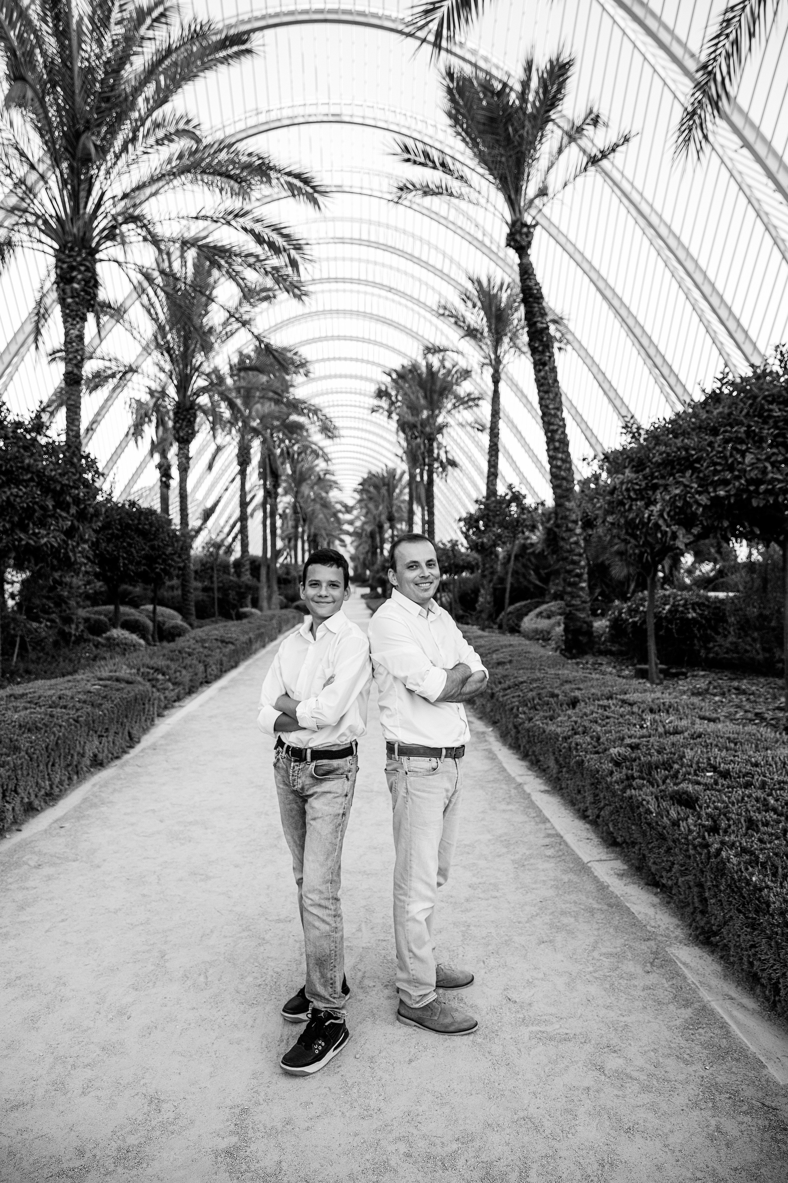 Padre e hijo de espaldas, con atuendos a juego, bajo el icónico arco de palmeras de la Ciudad de las Artes y las Ciencias en Valencia, España — una sesión familiar elegante y atemporal perfecta para quienes buscan retratos memorables de padre e hijo en Valencia y España.