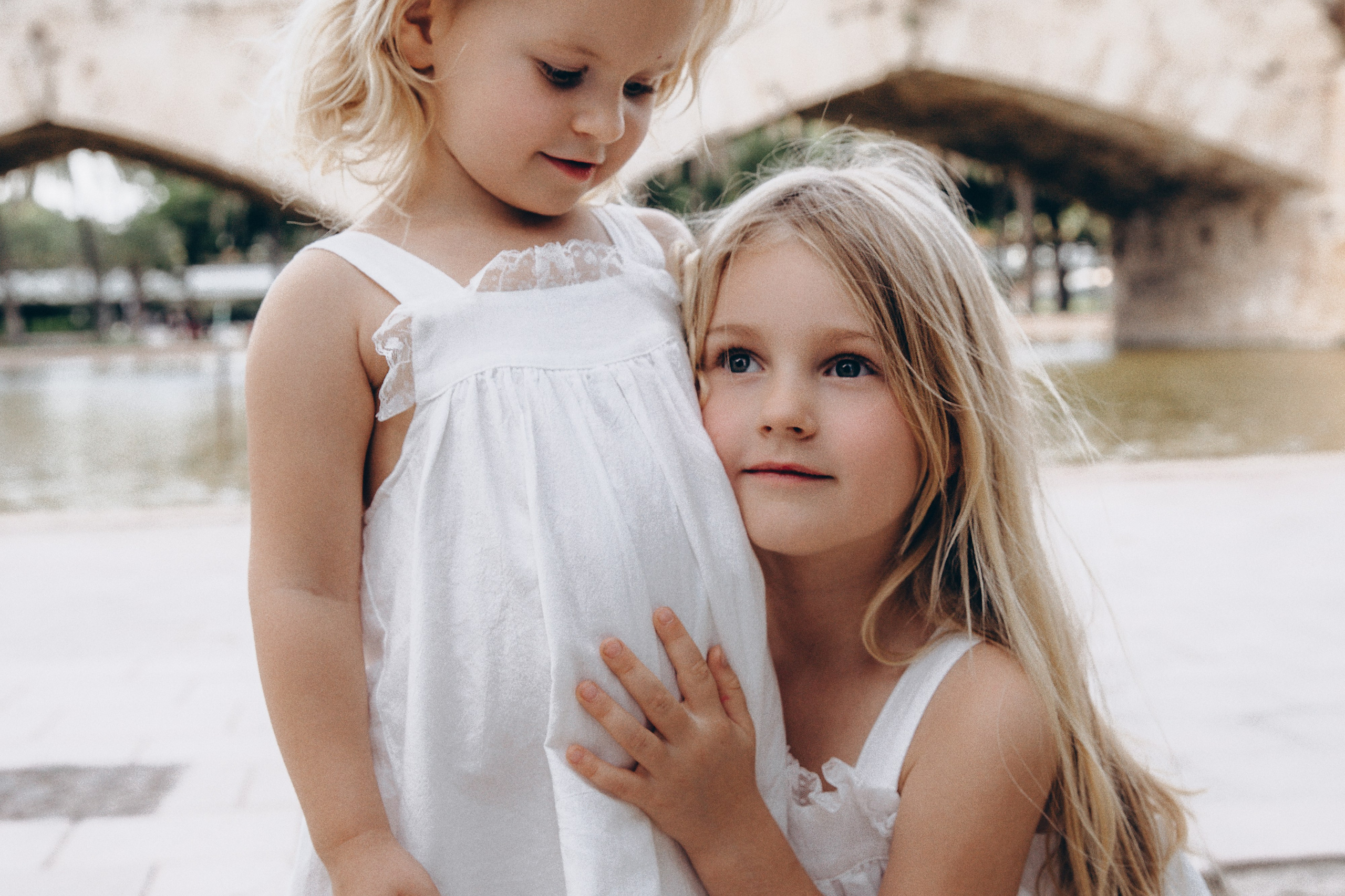 Primer plano de una foto familiar de dos hermanas con vestidos blancos compartiendo un momento tierno durante una sesión en Valencia, España — ideal para quienes buscan fotografía familiar amorosa y emocional en Valencia y en toda España, centrada en la conexión natural y la inocencia infantil.