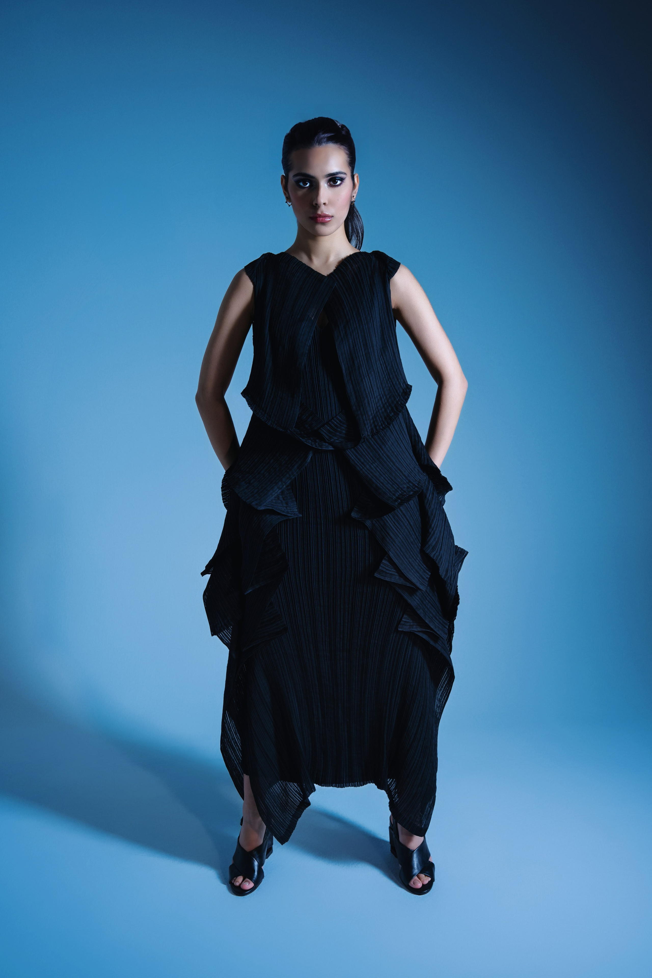 Futuristic Fashion Photography with Blue Lighting – A model striking a dynamic pose in a black outfit from Issey Miyake, captured in a modern fashion shoot using blue lighting to create an edgy, contemporary atmosphere