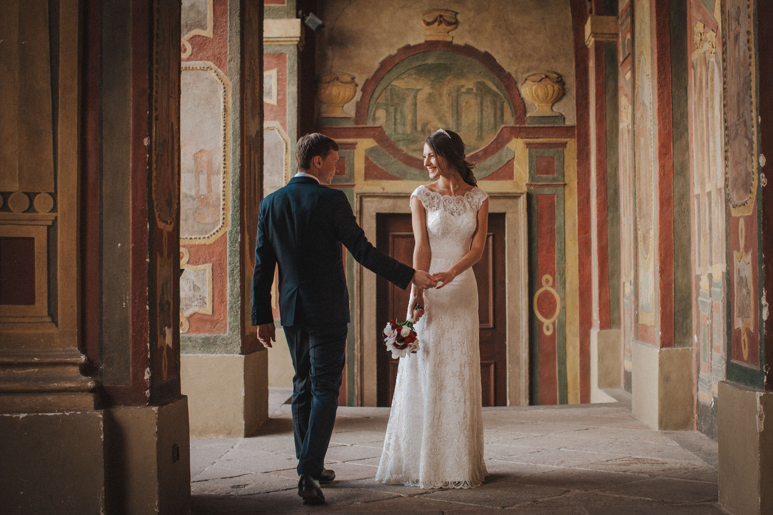 Russian groom holding Ukrainian bride's hand in historic Ledebour Garden, Prague, on wedding day.