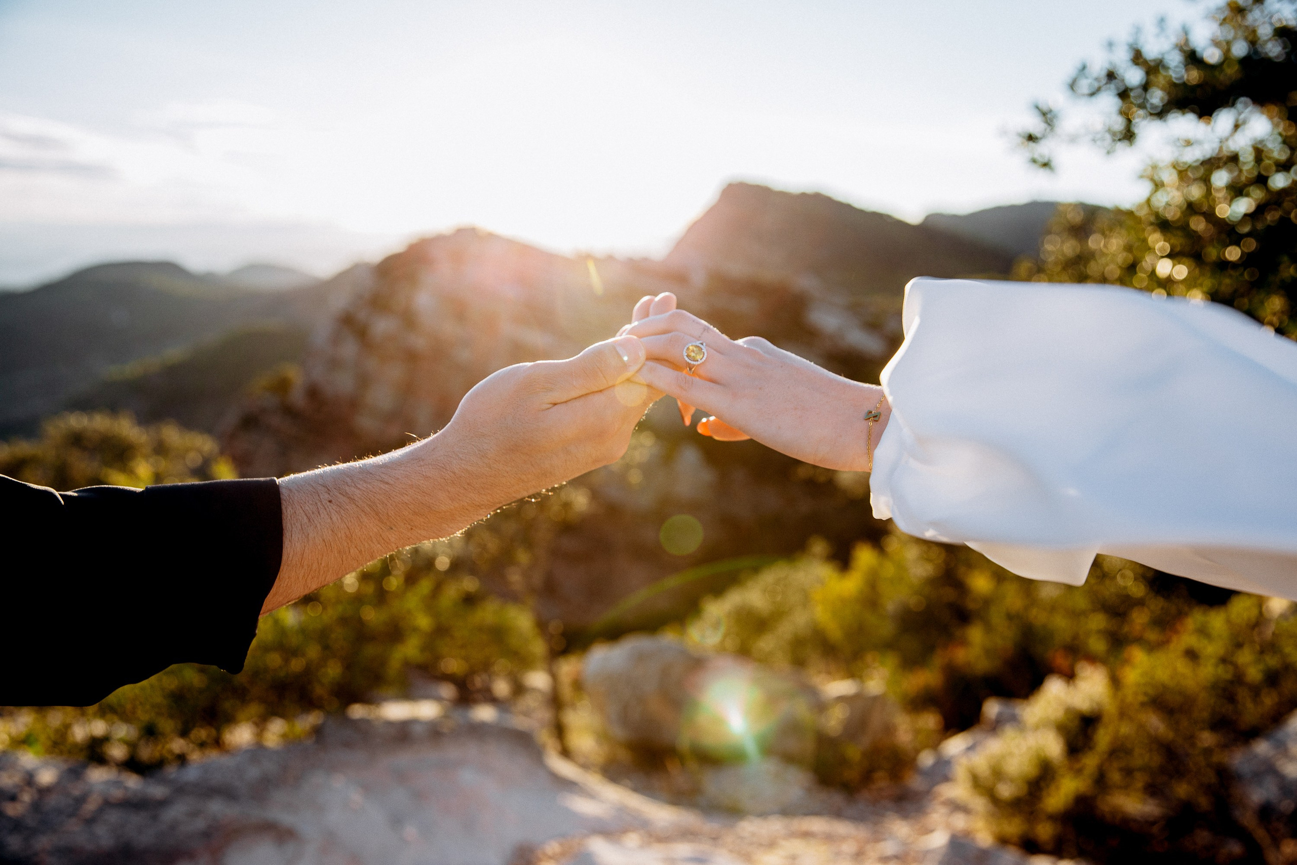Couple holding hands at golden hour on a mountain overlook during an intimate destination elopement in Barcelona, Spain. This romantic engagement-style moment captures the connection and emotion of a private civil wedding surrounded by nature.