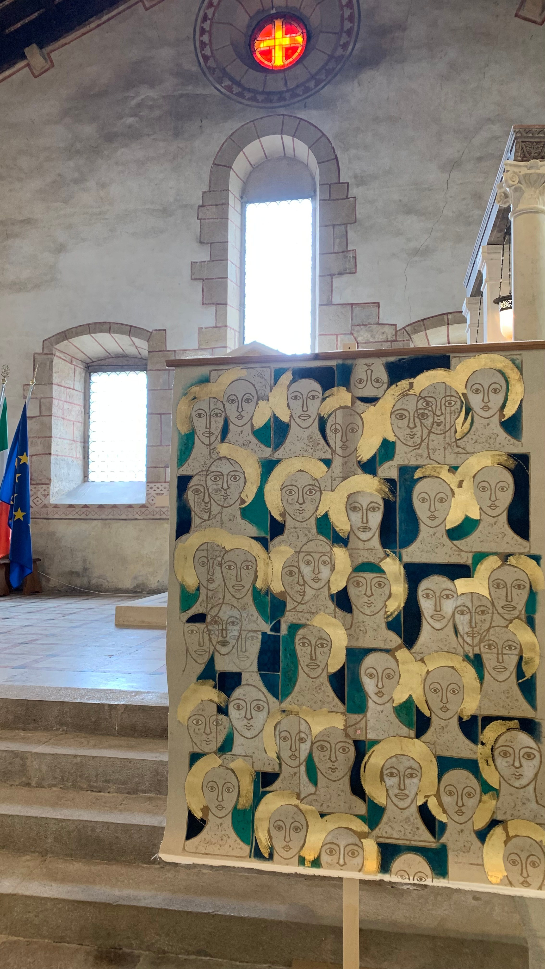 In HOLY FACES, Nadia Kuprina explores the theme of the icon through seriality and material stratification. The work originates from the repetition of three original linocuts, hand-printed in gold, and is subsequently transformed through hand stitching, oil painting, and applications of gold leaf.Its exhibition history — two abbey settings and one winery — highlights the versatility of the work, capable of engaging with spiritual, architectural, and unconventional exhibition spaces. The publication in a catalogue reinforces its curatorial relevance and the solidity of the artist’s trajectory.