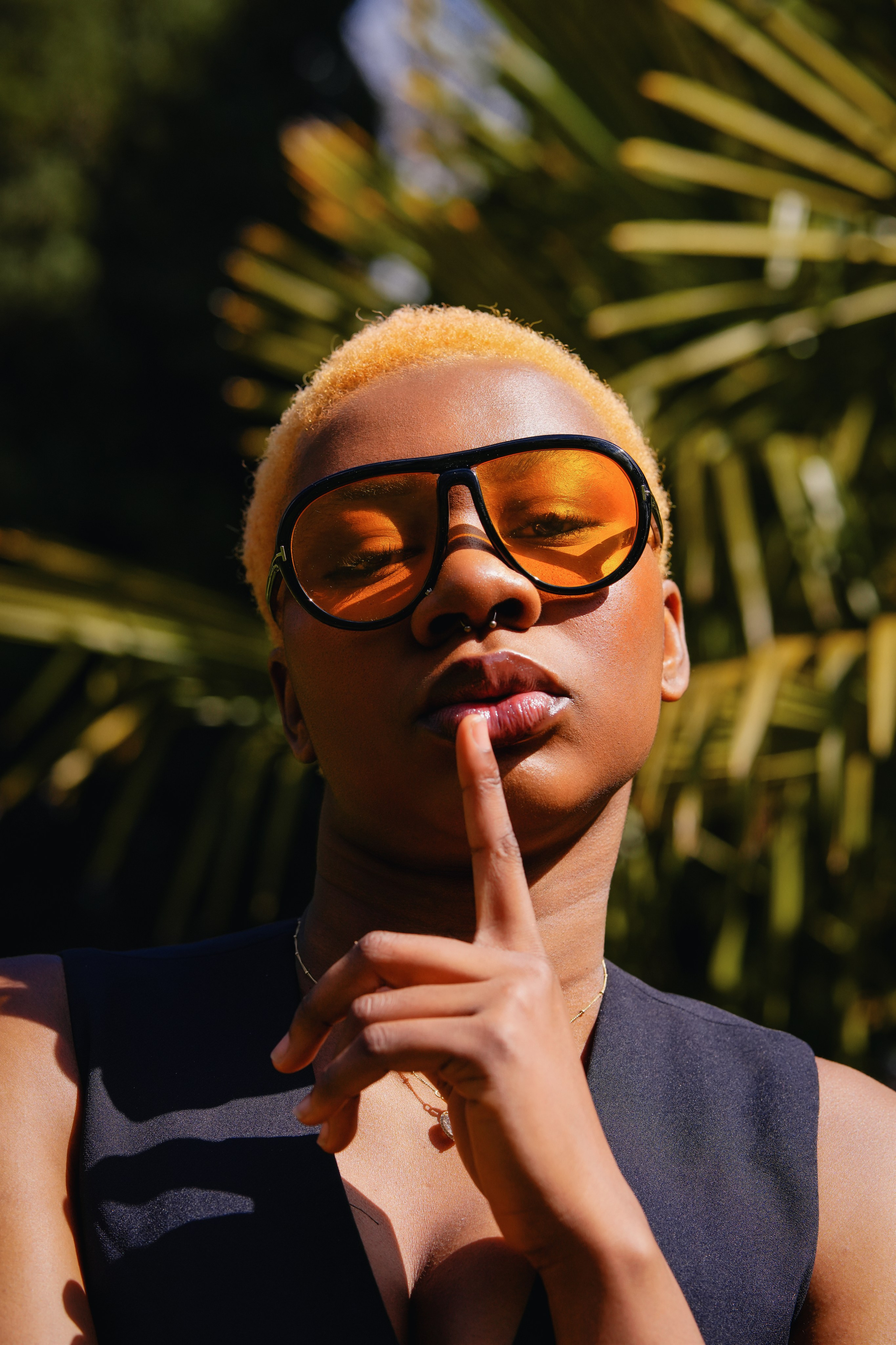 Outdoor portrait of a woman in a black dress surrounded by greenery, photographed in a clean editorial style with soft natural light.