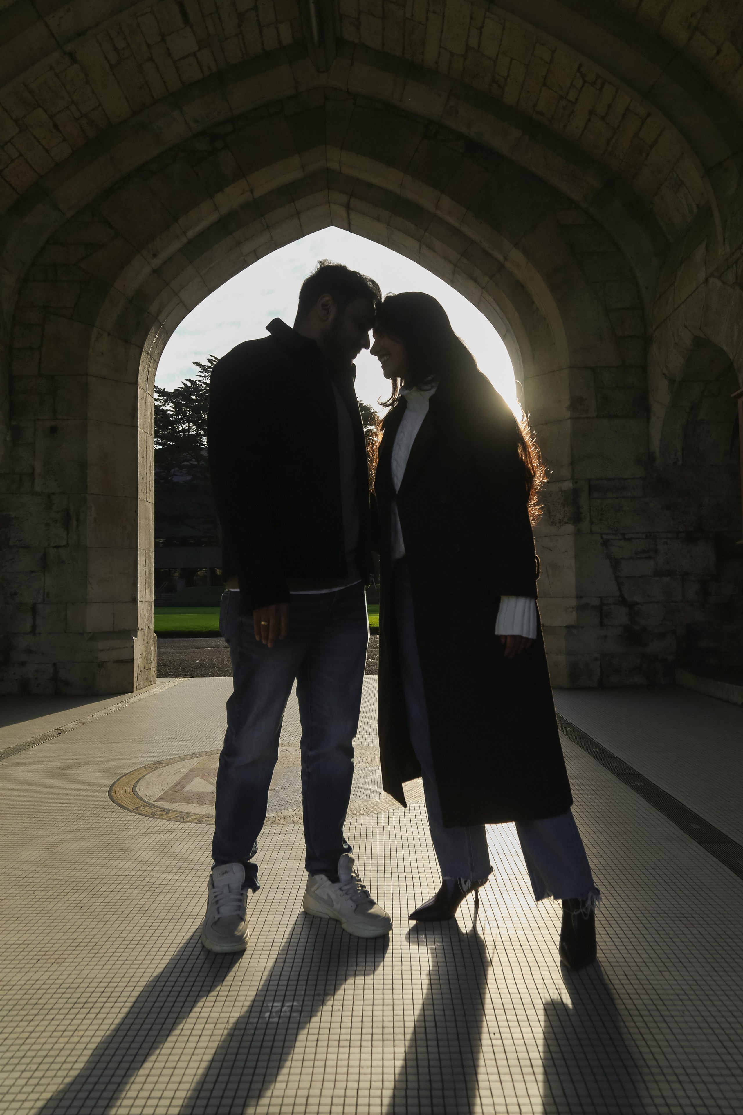 A dramatic silhouette framed by stone arches and soft backlight, emphasizing shape, connection, and timeless atmosphere.