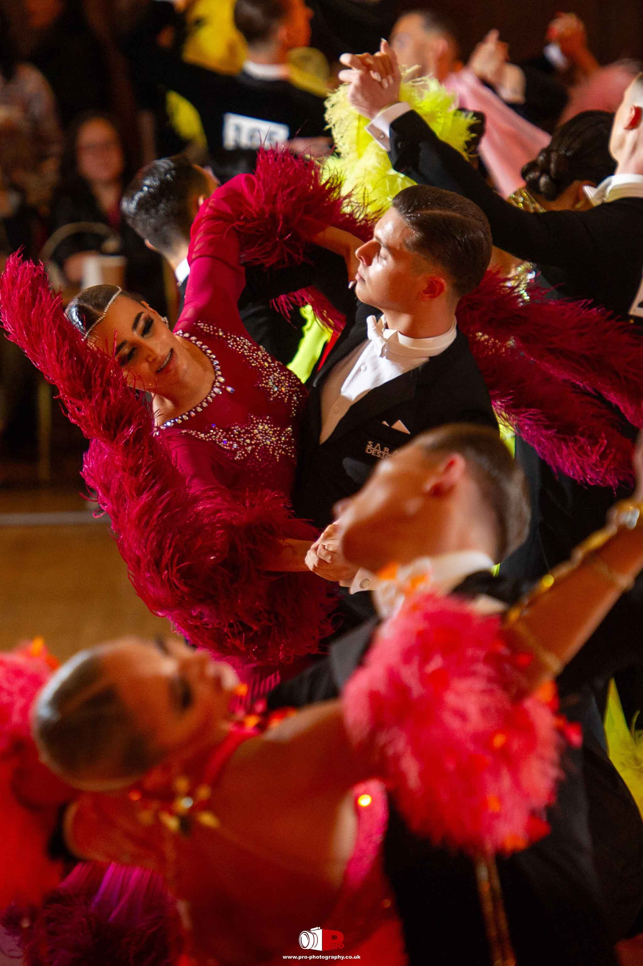 Elegant ballroom dancers in vibrant red feathered outfits performing a dynamic routine on a dance floor