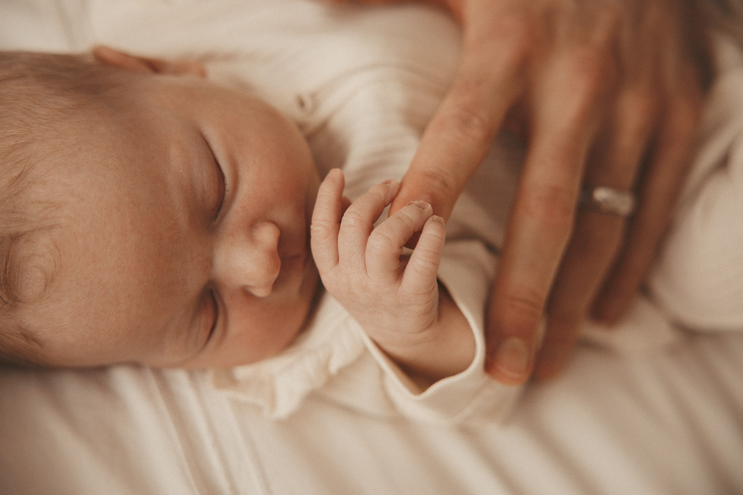 Sleeping newborn baby with parent’s gentle hand nearby