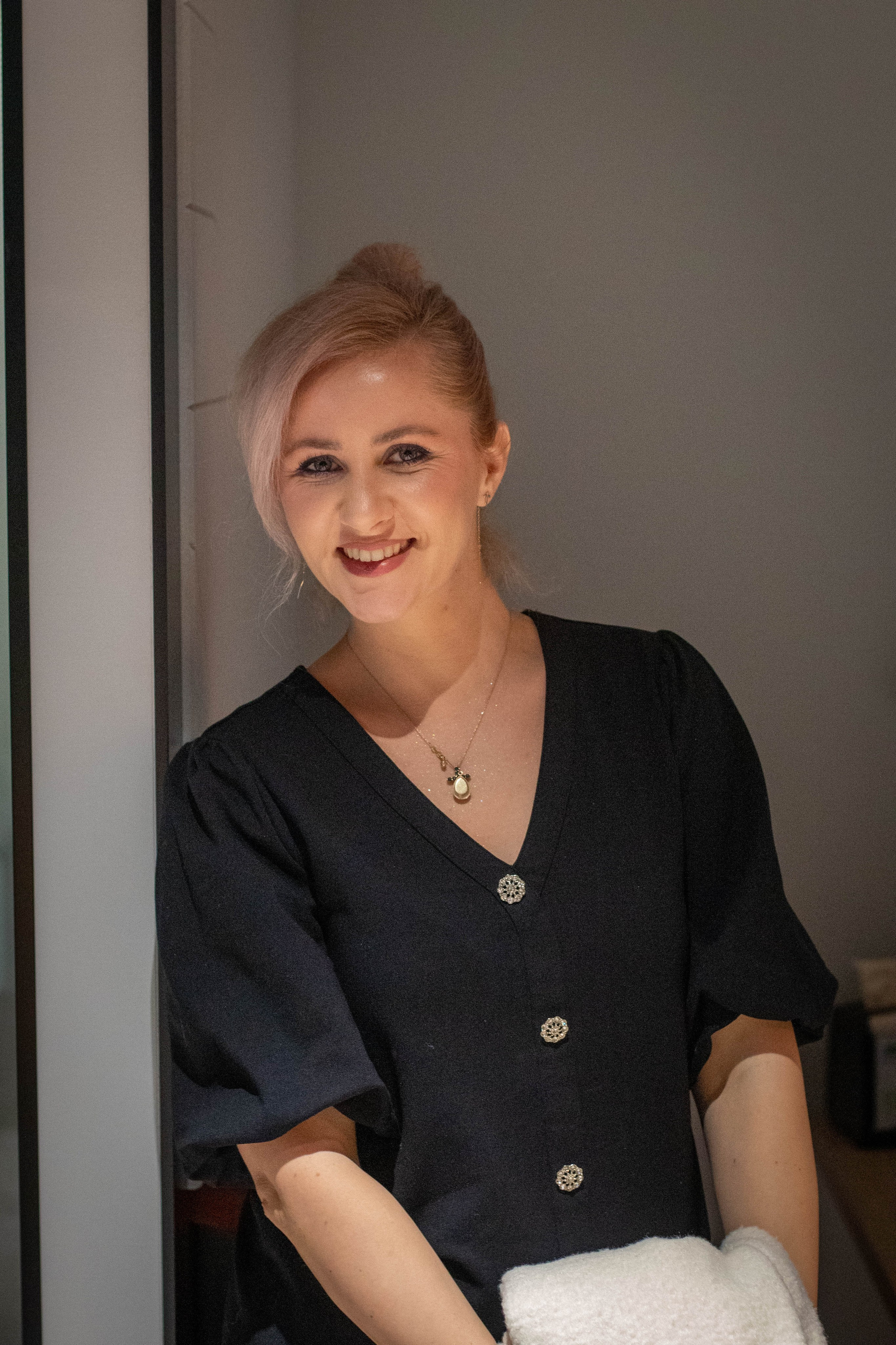 Stylish woman in black shirt leaning against a wall with a confident expression, indoor portrait.