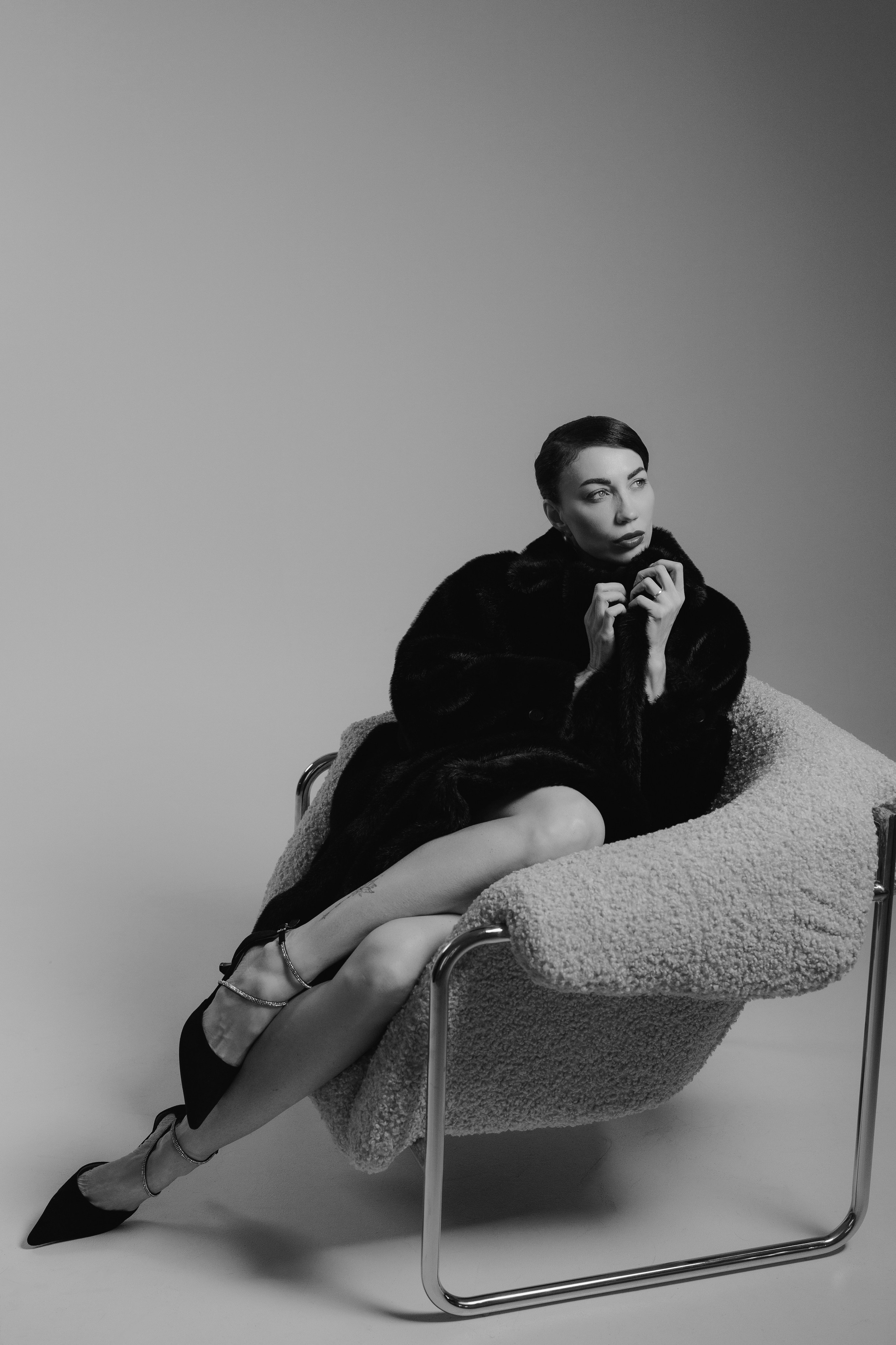 Minimalist fashion portrait of a woman in a black fur coat with elegant pose and dramatic shadows in studio, photographed in Leipzig, Germany. Минималистичный фэшн-портрет девушки в чёрной шубе с элегантной позой и драматичными тенями в студии, снятый в Лейпциге, Германия.