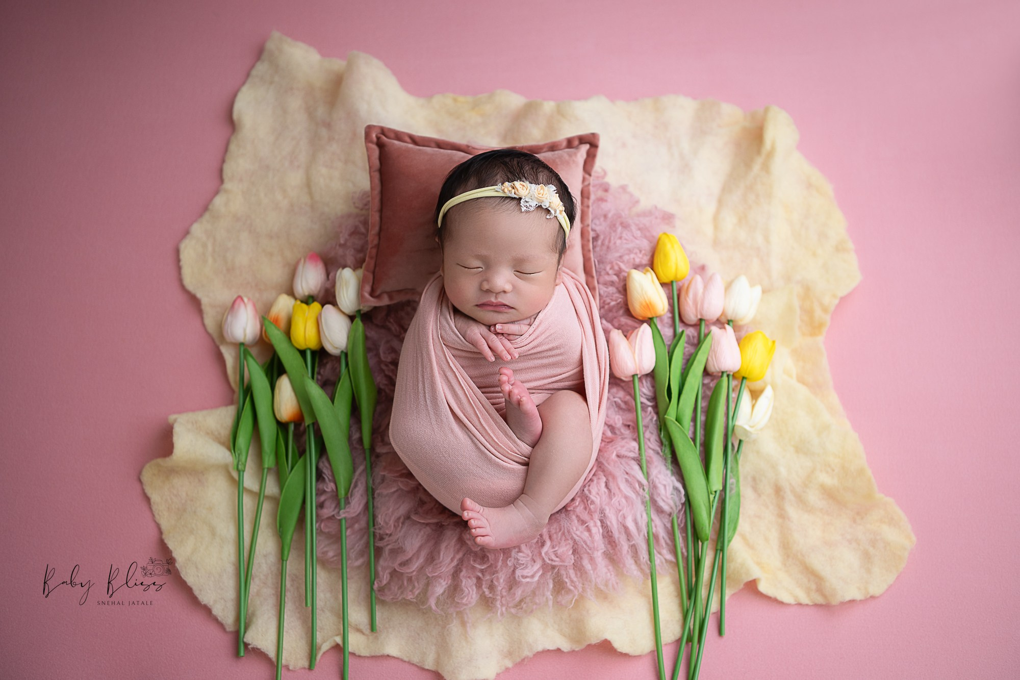 tulip colourful flowers as a background for newborn baaby girl in dusky pink outfit.