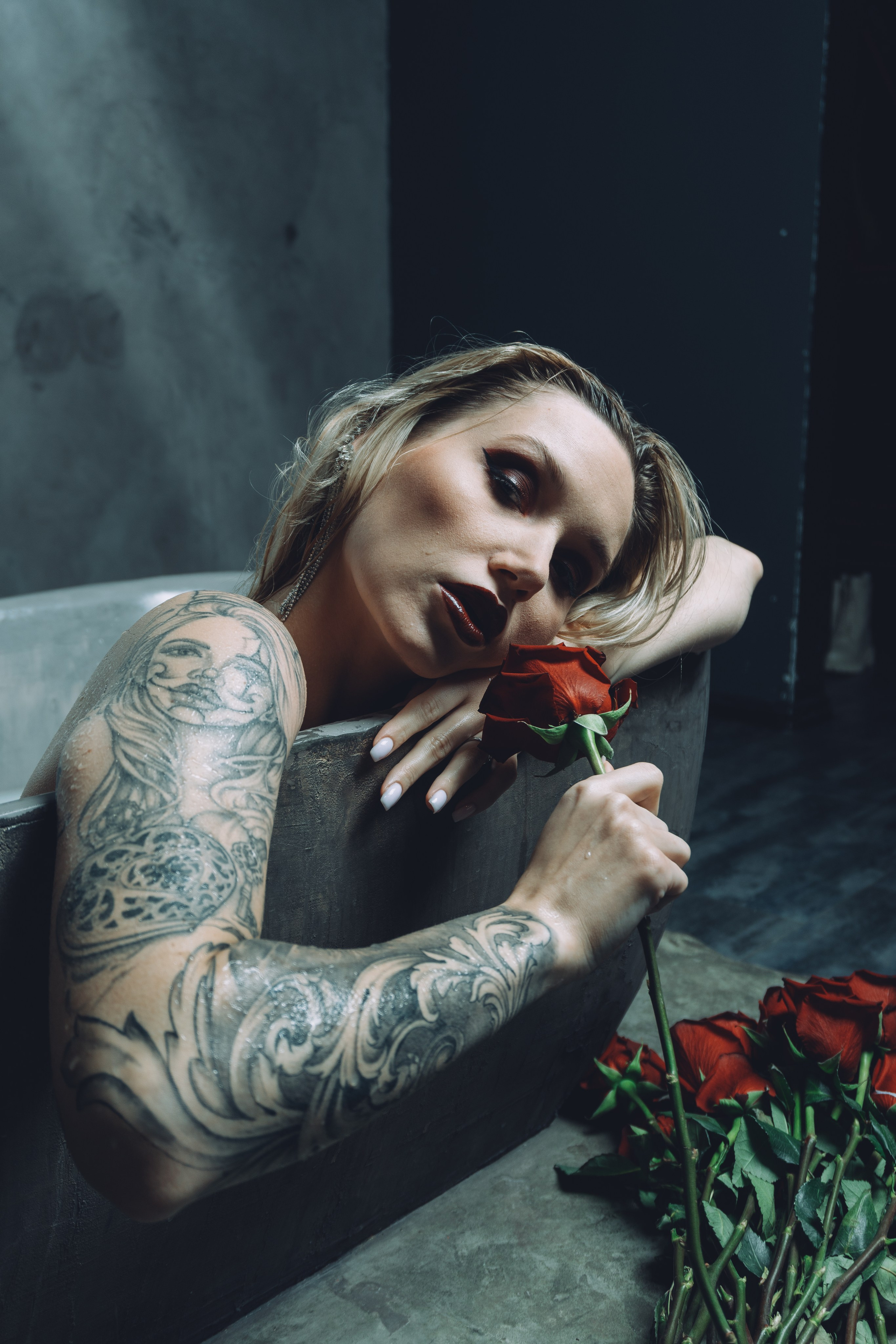 Woman with tattoos holding a bouquet of flowers in a bath with white water.
