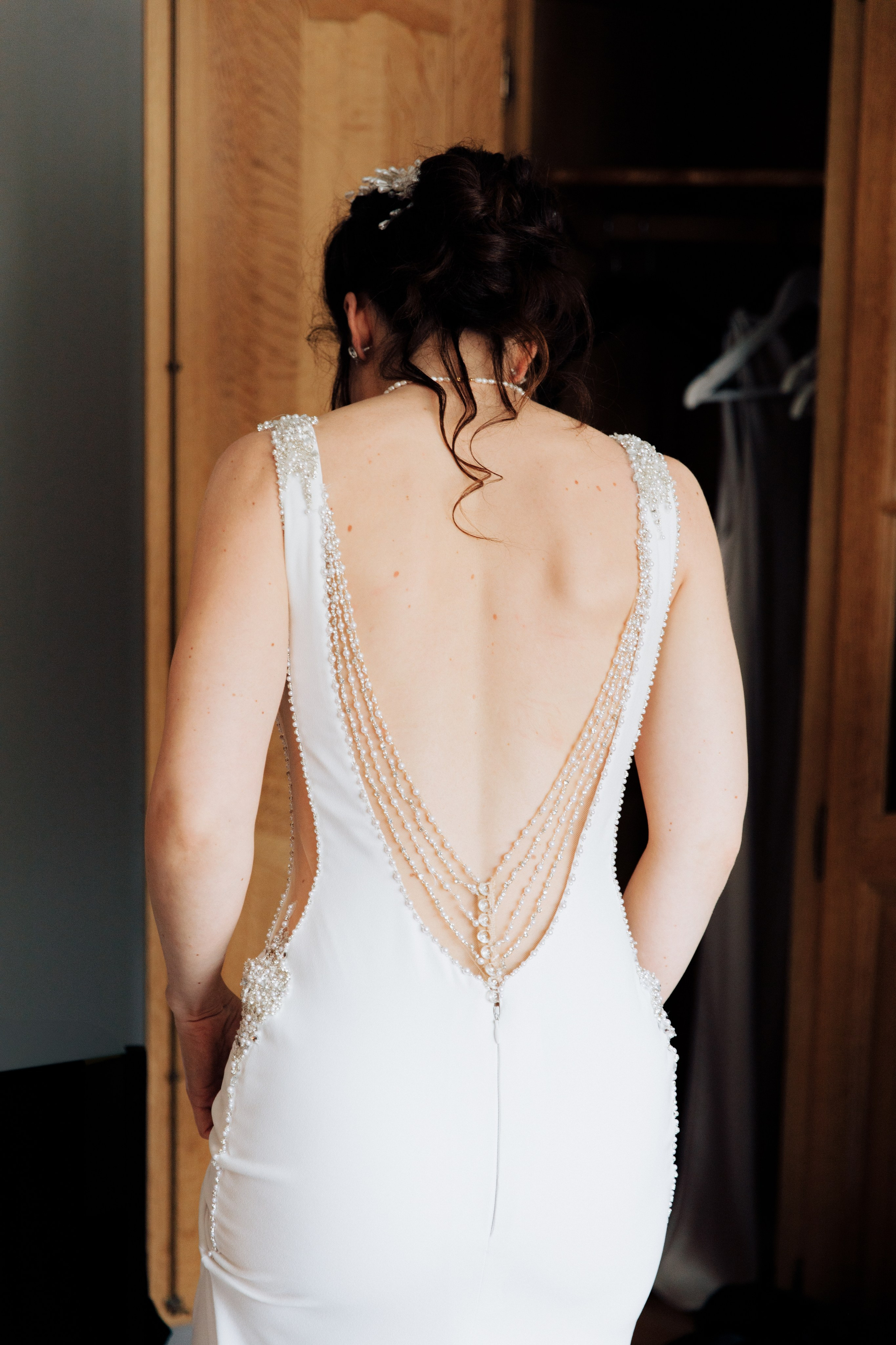 Die Braut steht mit dem Rücken zu uns und wir sehen ihren schönen, offenen Rücken im Hochzeitskleid