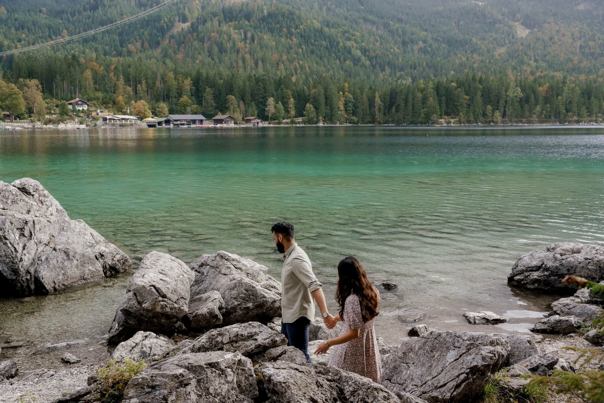 Wide shot of couple on rocks at Eibsee with turquoise water and Zugspitze mountains in the background