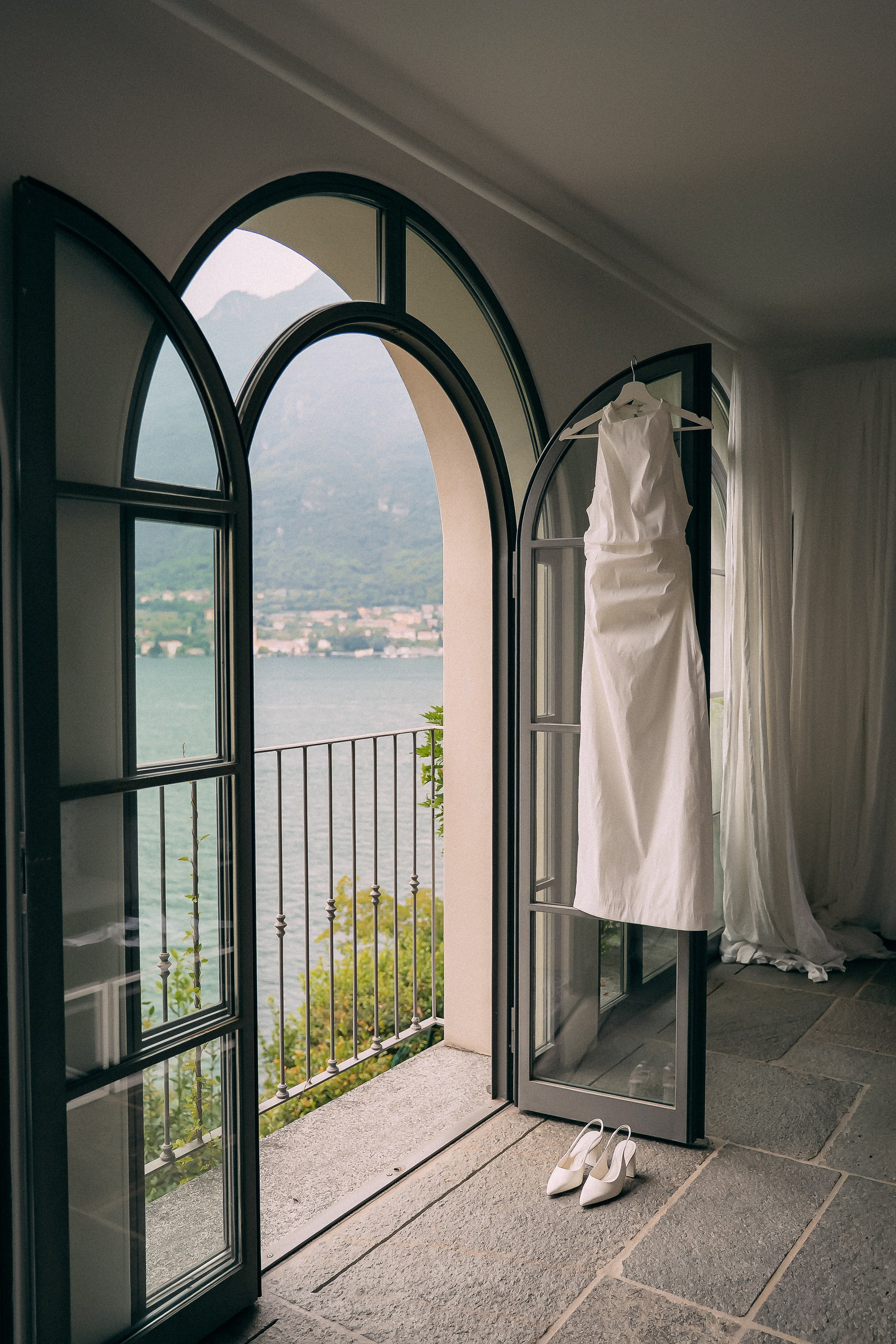 Wedding dress hanging in an arched doorway overlooking Lake Como, Italy