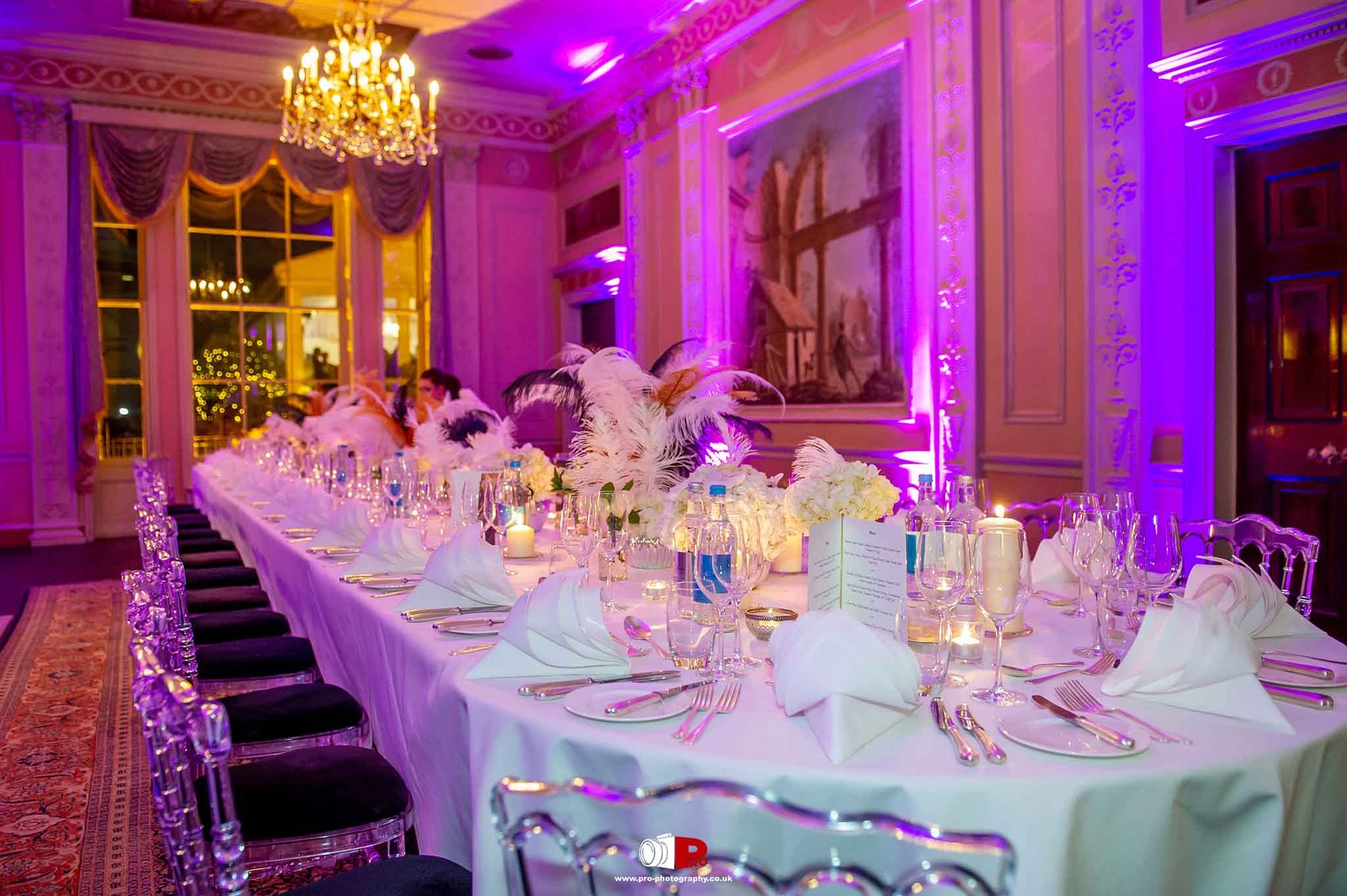 A lavishly decorated dining hall with chandeliers, feather centerpieces, and an elegant table setting at a private event.