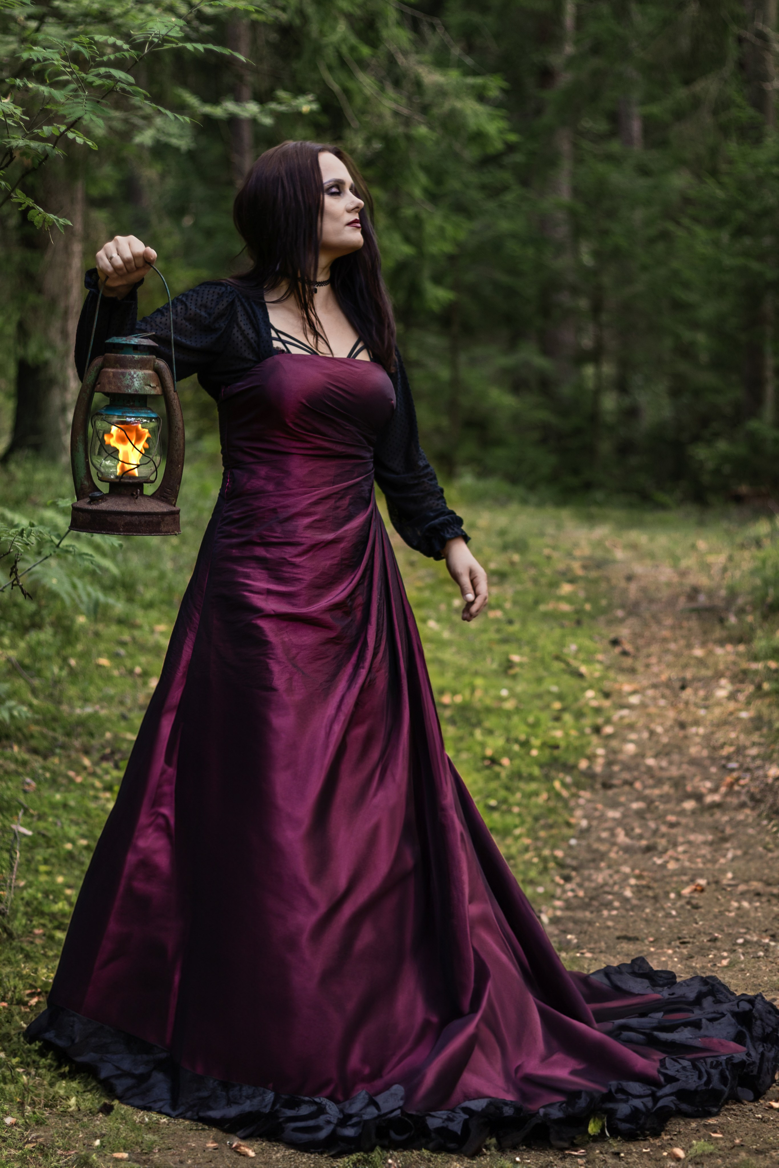 Девушка-ведьма в черном одеянии держит горящий факел в руках.