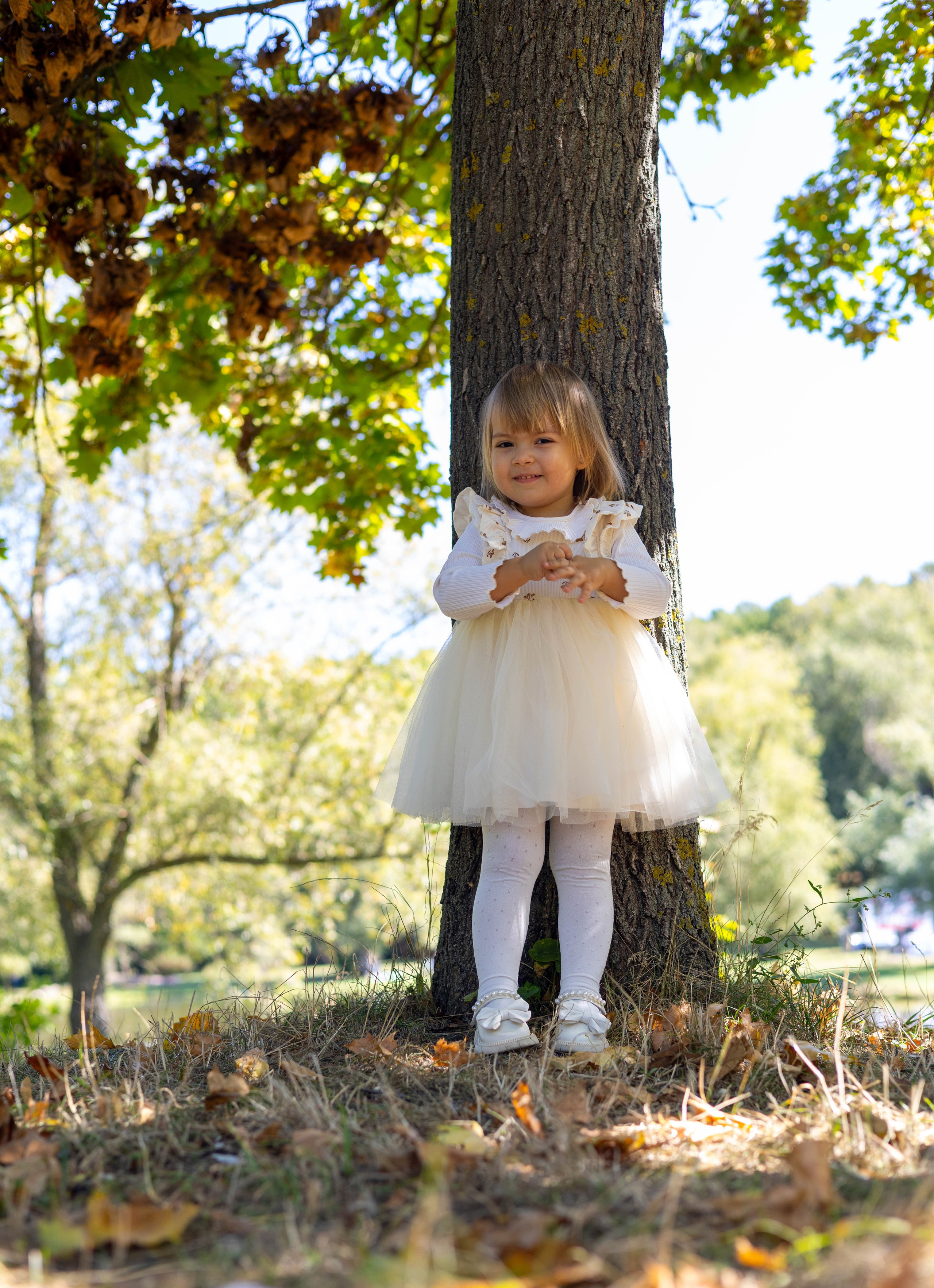 Маленькая девочка в белом платье возле дерева