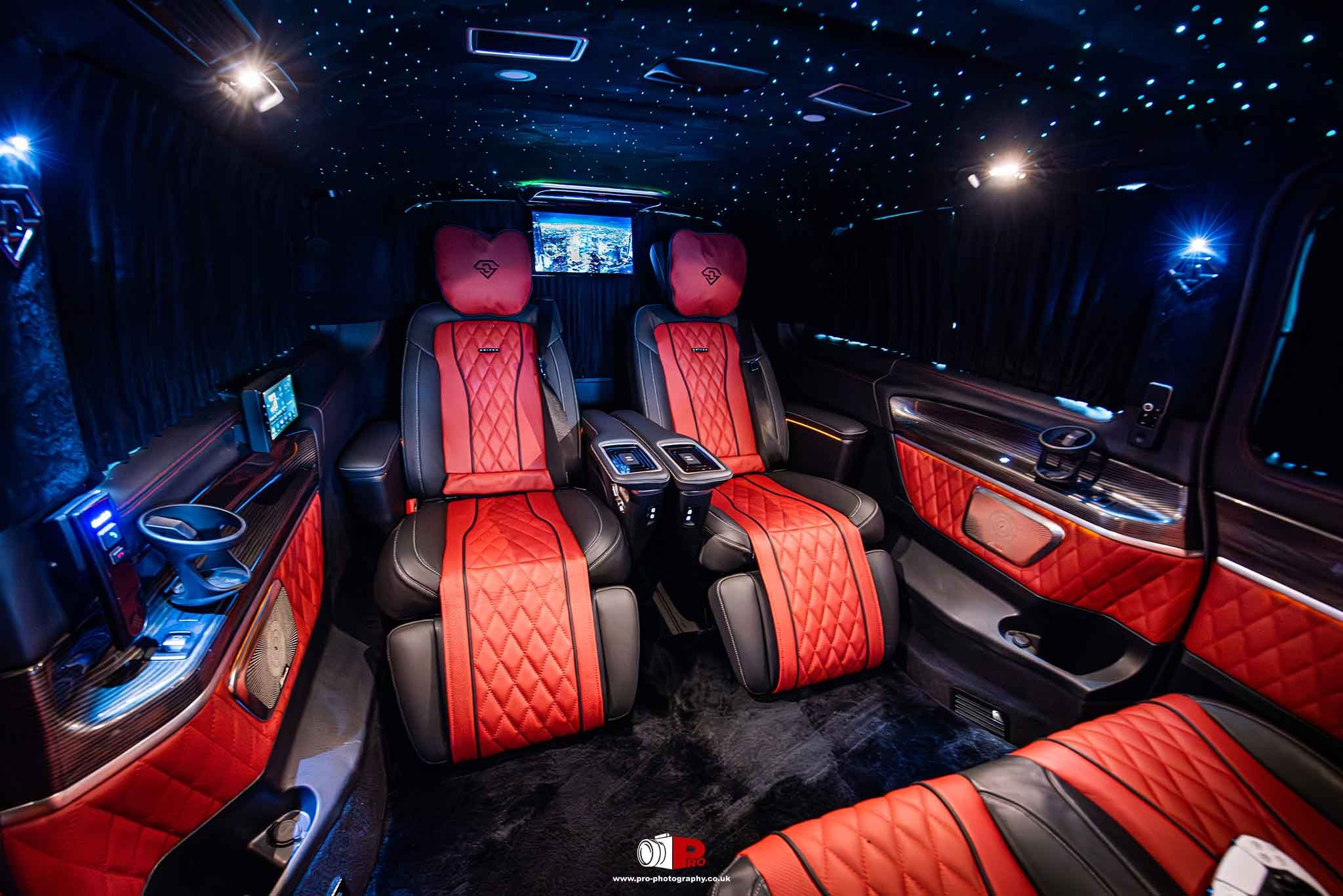 Opulent car interior featuring red quilted leather seats, ambient lighting, and a sleek entertainment setup.