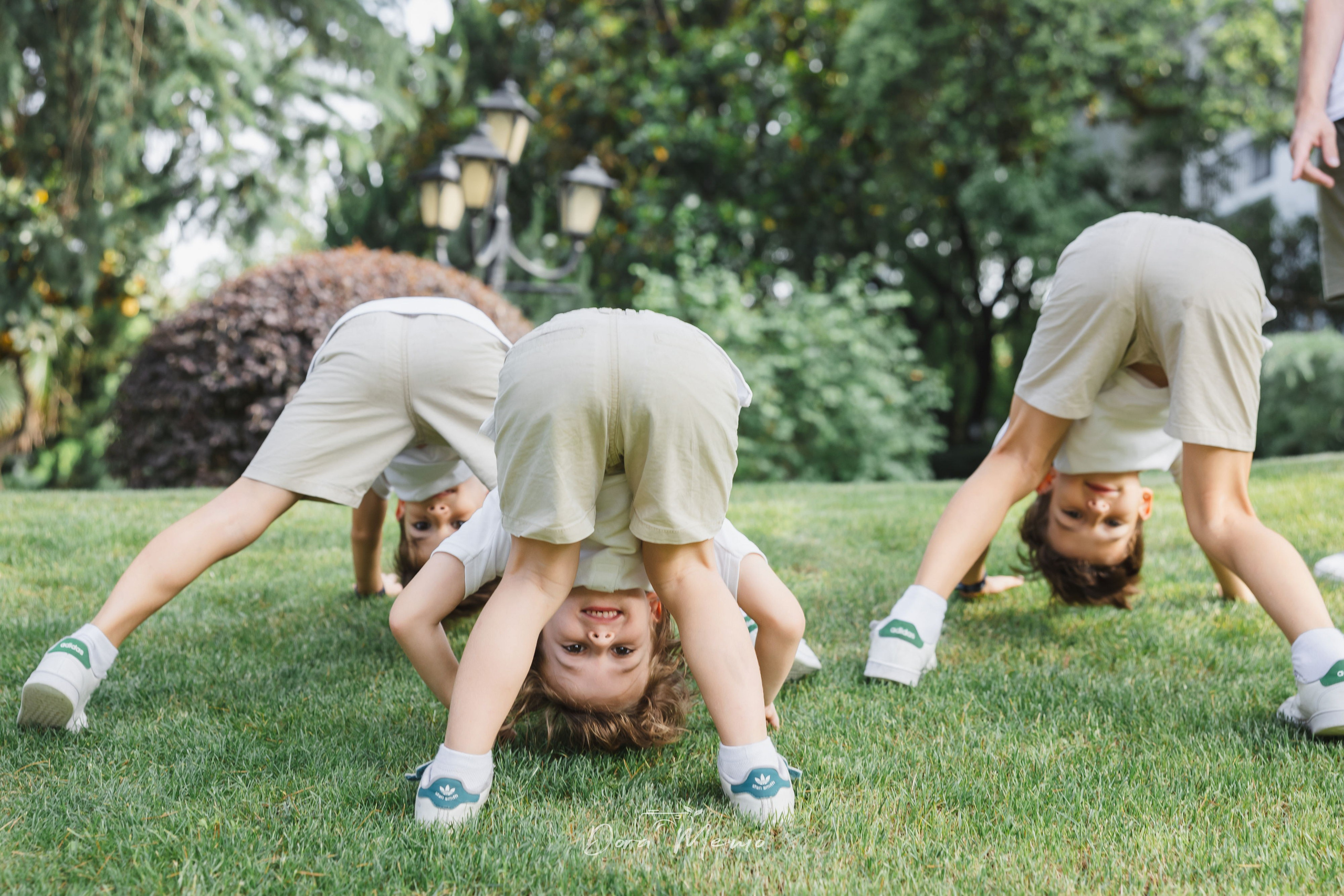 Three kids doing somersaults on grass | Three children tumbling on the grass together, sibling fun