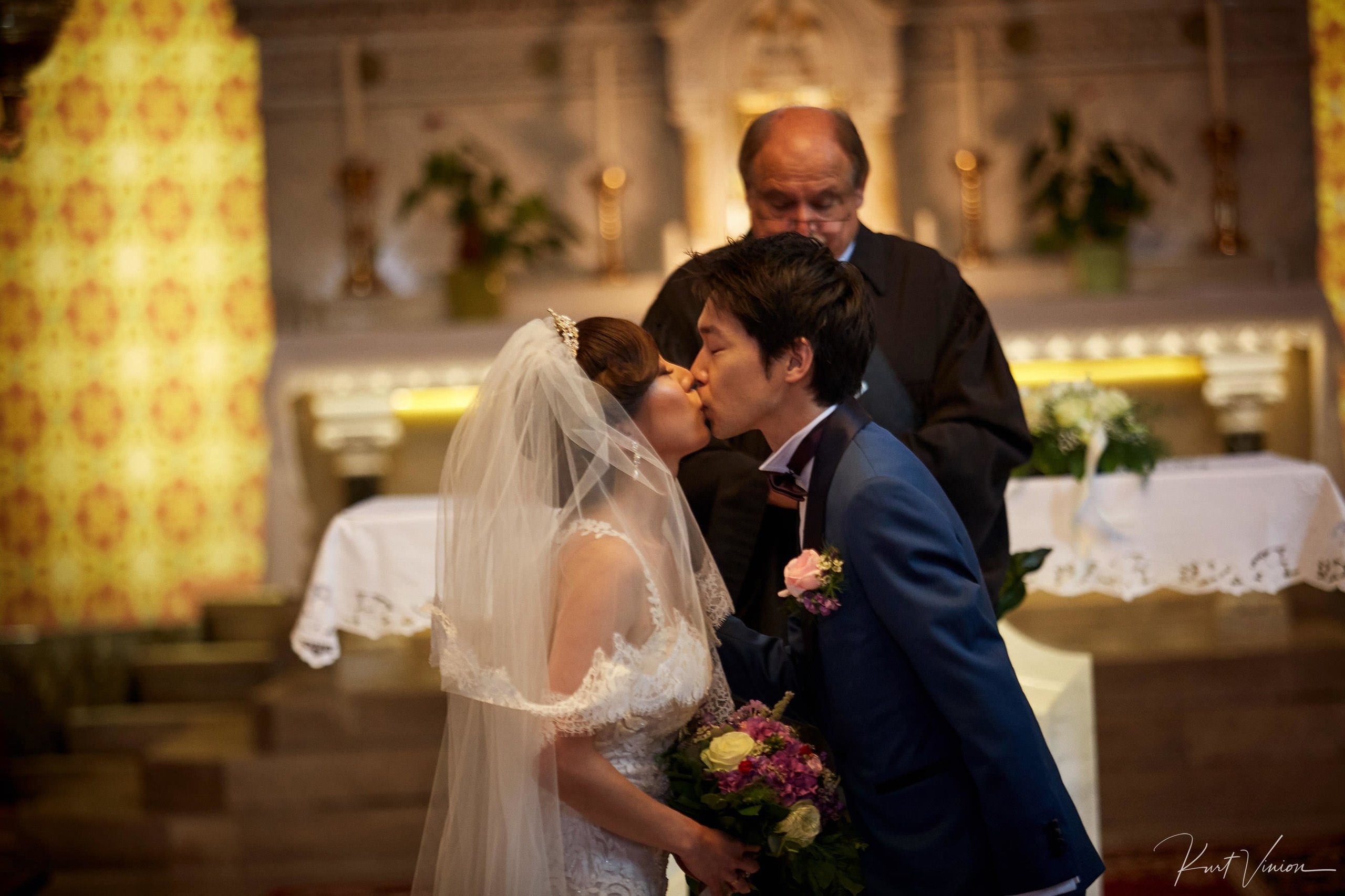 Newlyweds sharing holy kiss watched by priest Bled ceremony.