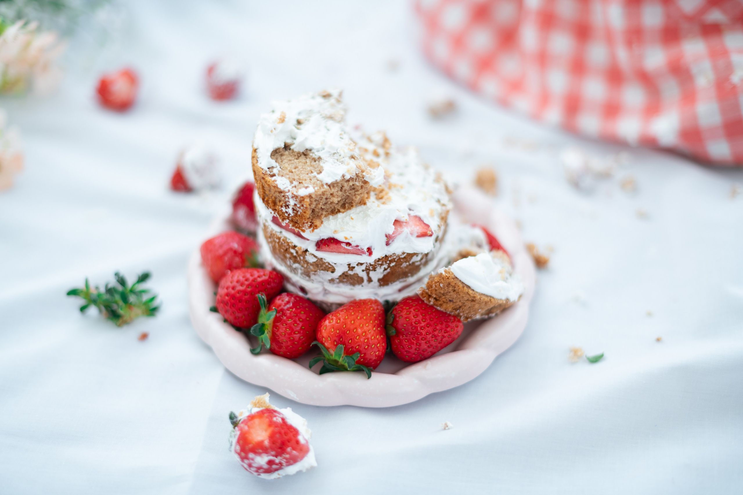 Messy strawberry shortcake—layers split, cream and crumbs everywhere, fresh berries circling a pink plate.