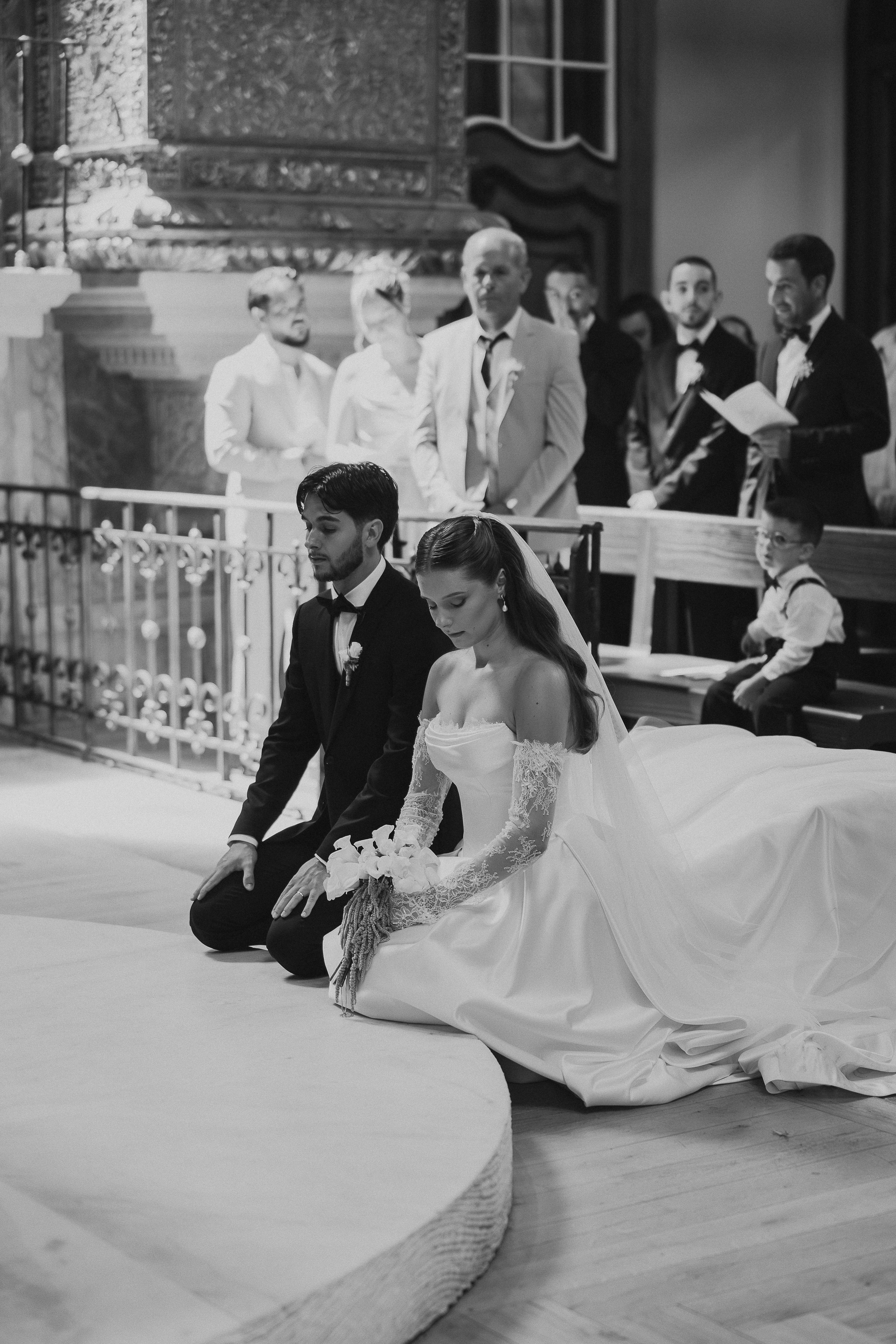 Noivos ajoelhados perante o altar em fotografia a preto e branco