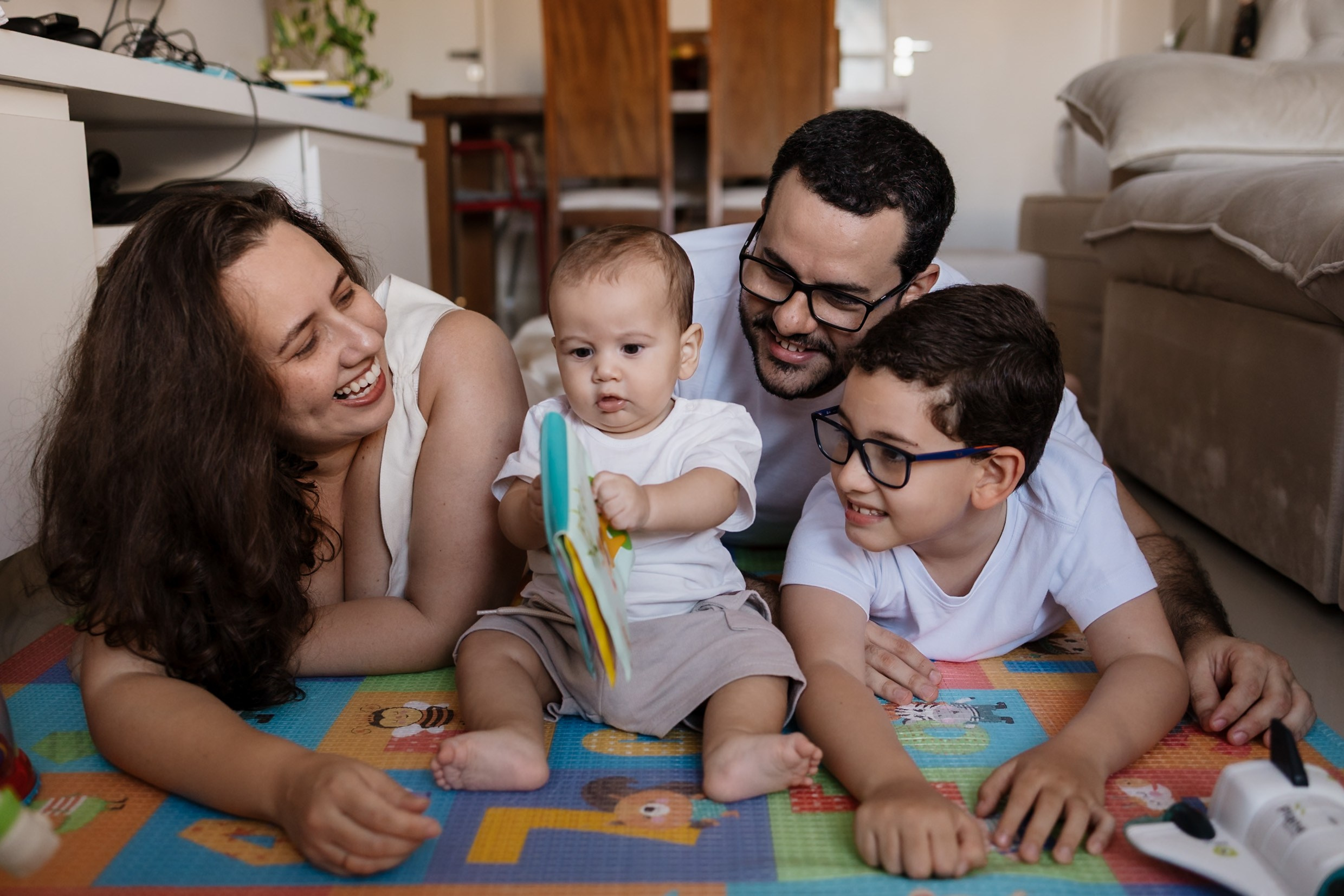 Família junta no chão da casa durante ensaio familiar.