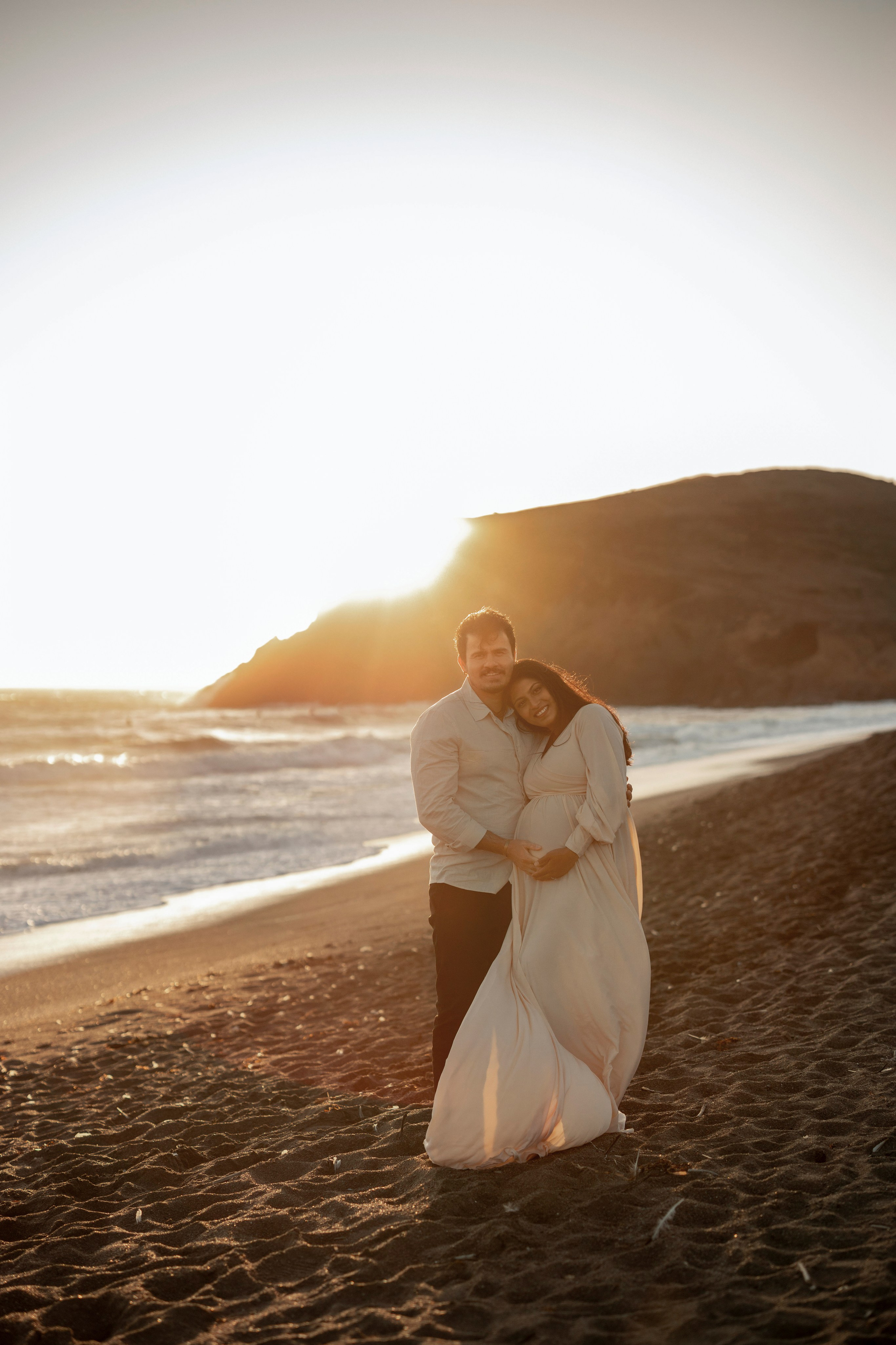 Maternity photoshoot on the beach with expecting parents embracing at sunset