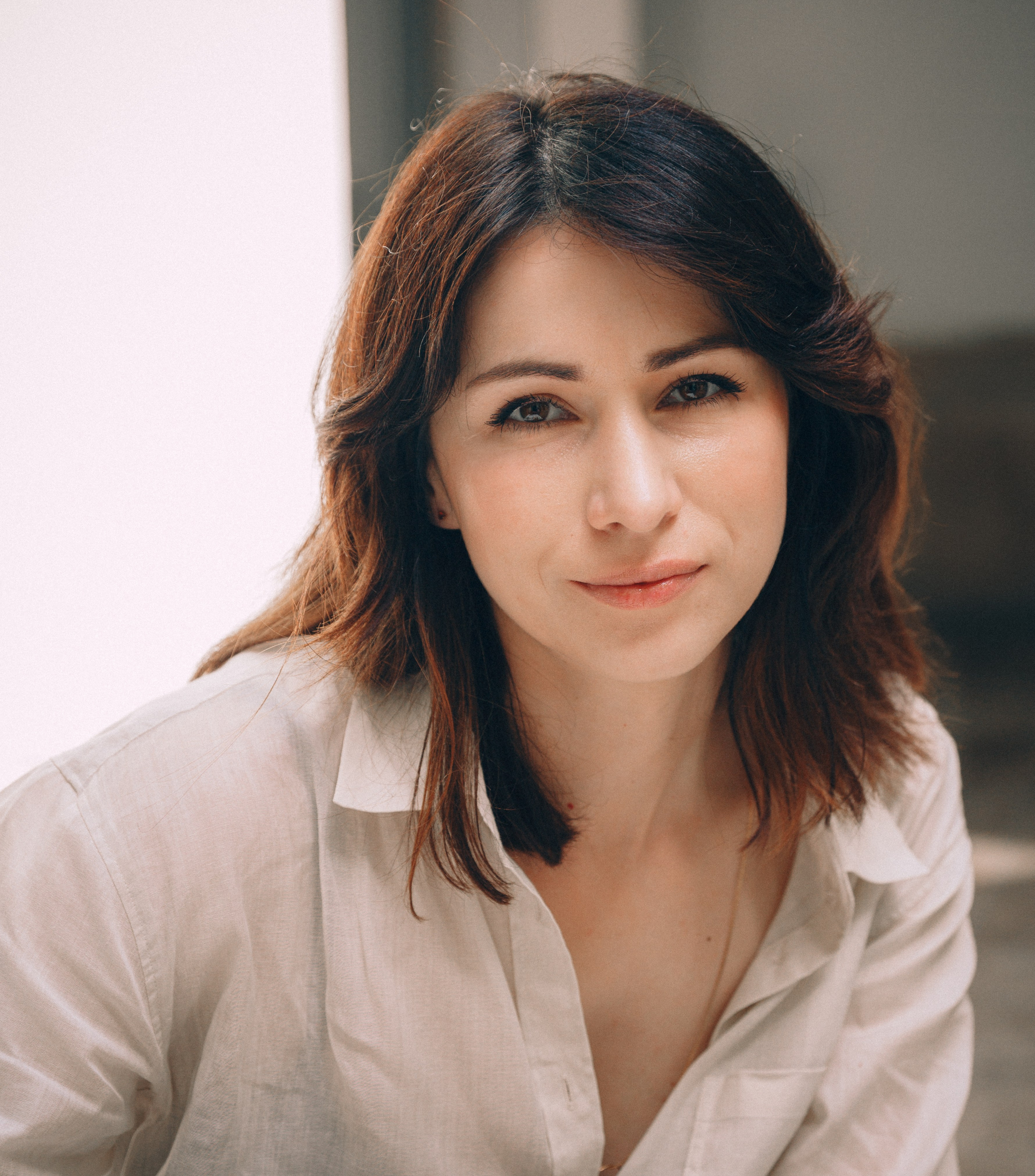 Крупный портрет при естественном освещении женщины с мягкими волнами волос и белой рубашкой, спокойно смотрящей в камеру в Кальпе, Испания — аутентичная и элегантная портретная фотография, подчеркивающая природную красоту и теплые тона, идеально подходит для профессиональных портретных фотосессий в Кальпе и Испании.