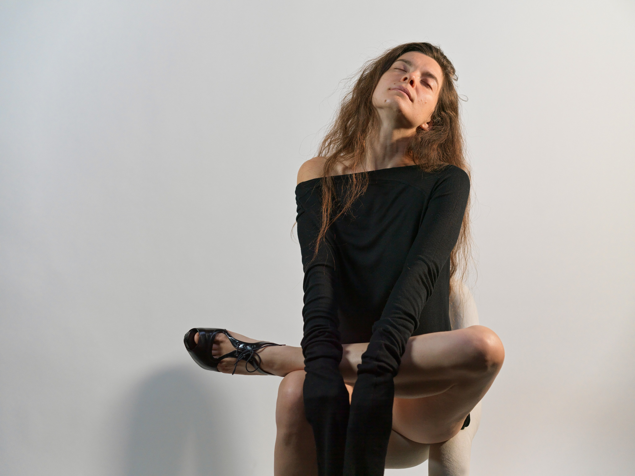 Model sitting provocatively on a chair, showcasing her long, toned legs and seductive high heels, captured in Milan or Verona, exuding confidence and allure