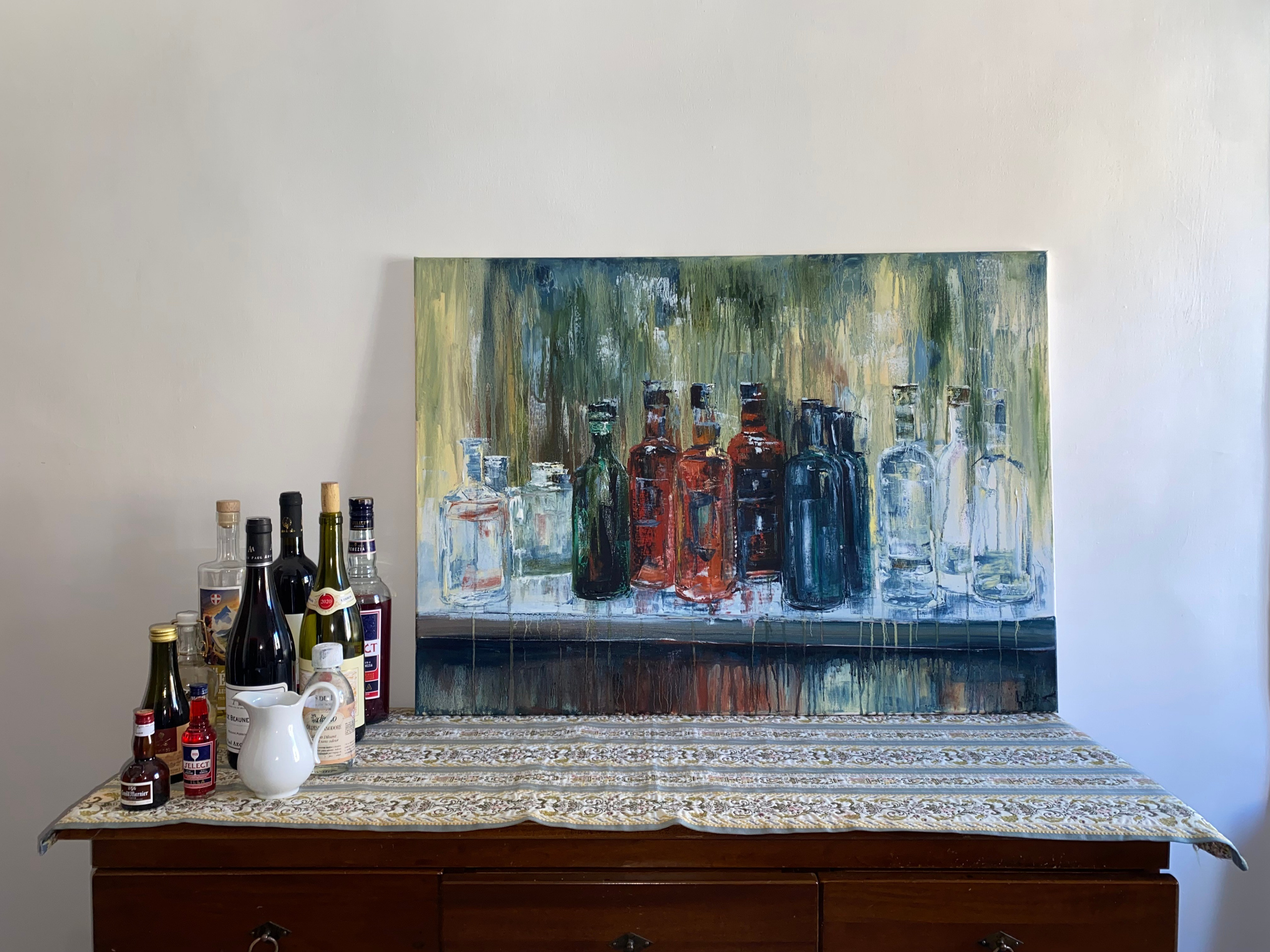 Expressive acrylic still life of a bar table with bottles, wine glasses, and a patterned tablecloth, rendered in warm reds and deep greens. Painting by Ekaterina Solopova addressing rituals of drinking and shared moments in bars restaurants and aperitivo time.