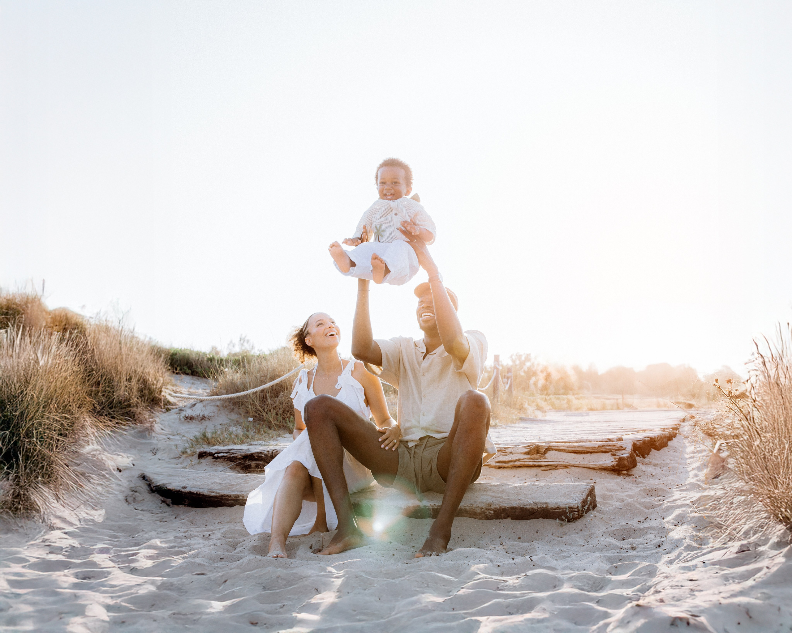 Alegre sesión familiar en la playa de Barcelona, España — padres sonrientes jugando con su hijo pequeño durante la hora dorada, capturando risas, conexión y luz natural. Ideal para quienes buscan sesiones familiares espontáneas y emotivas en Barcelona y la costa española.
