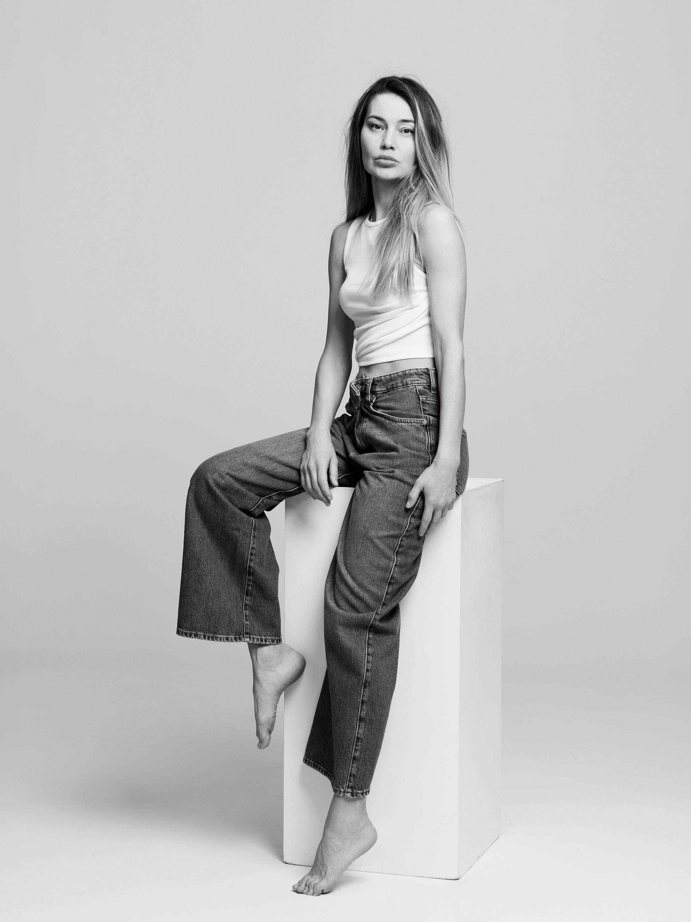 teenage girl sitting on a studio cube in jeans, black and white portrait