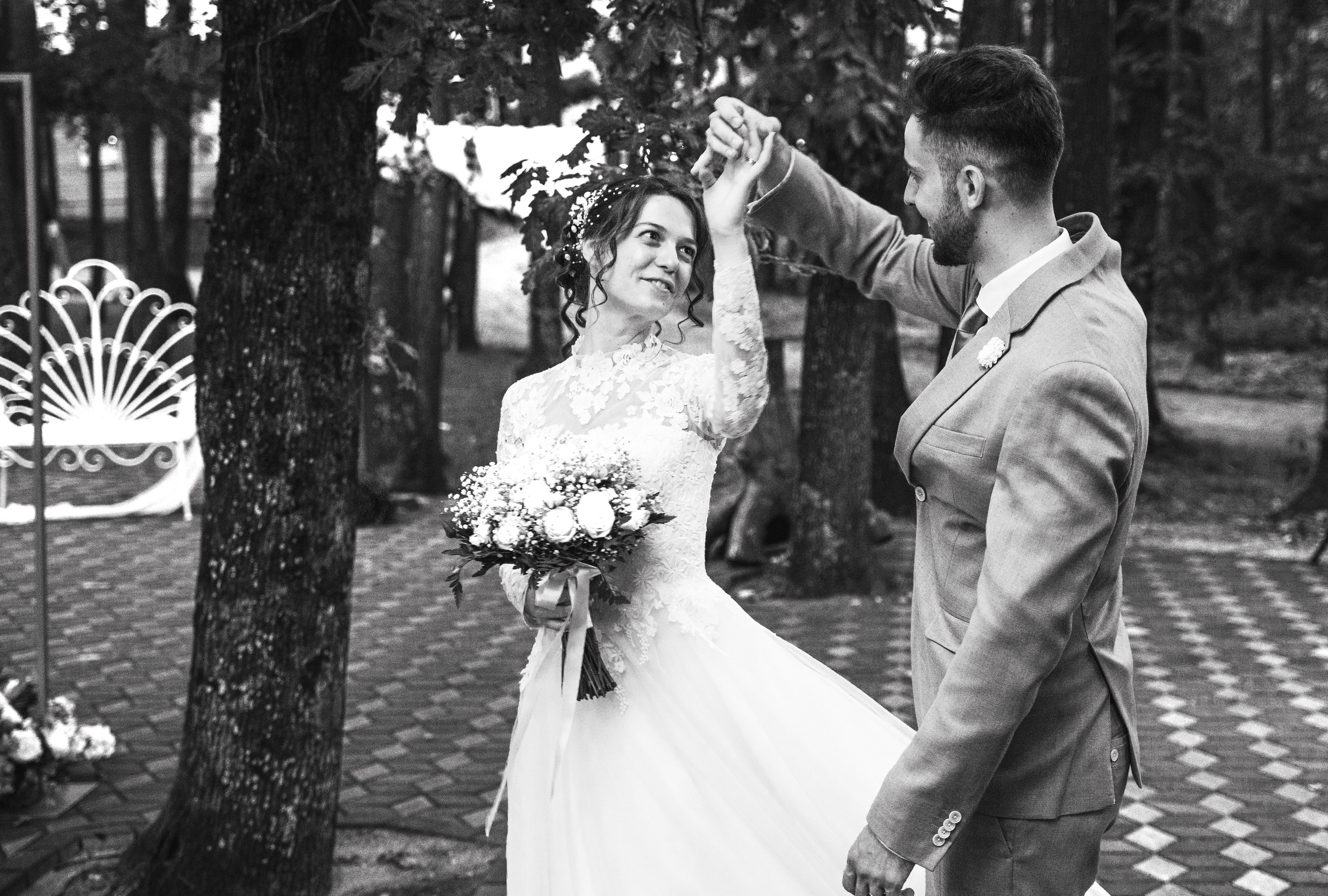 Fotografie alb-negru cu mirii dansând în aer liber, mireasa ținând buchetul și zâmbind, incadru.ro.