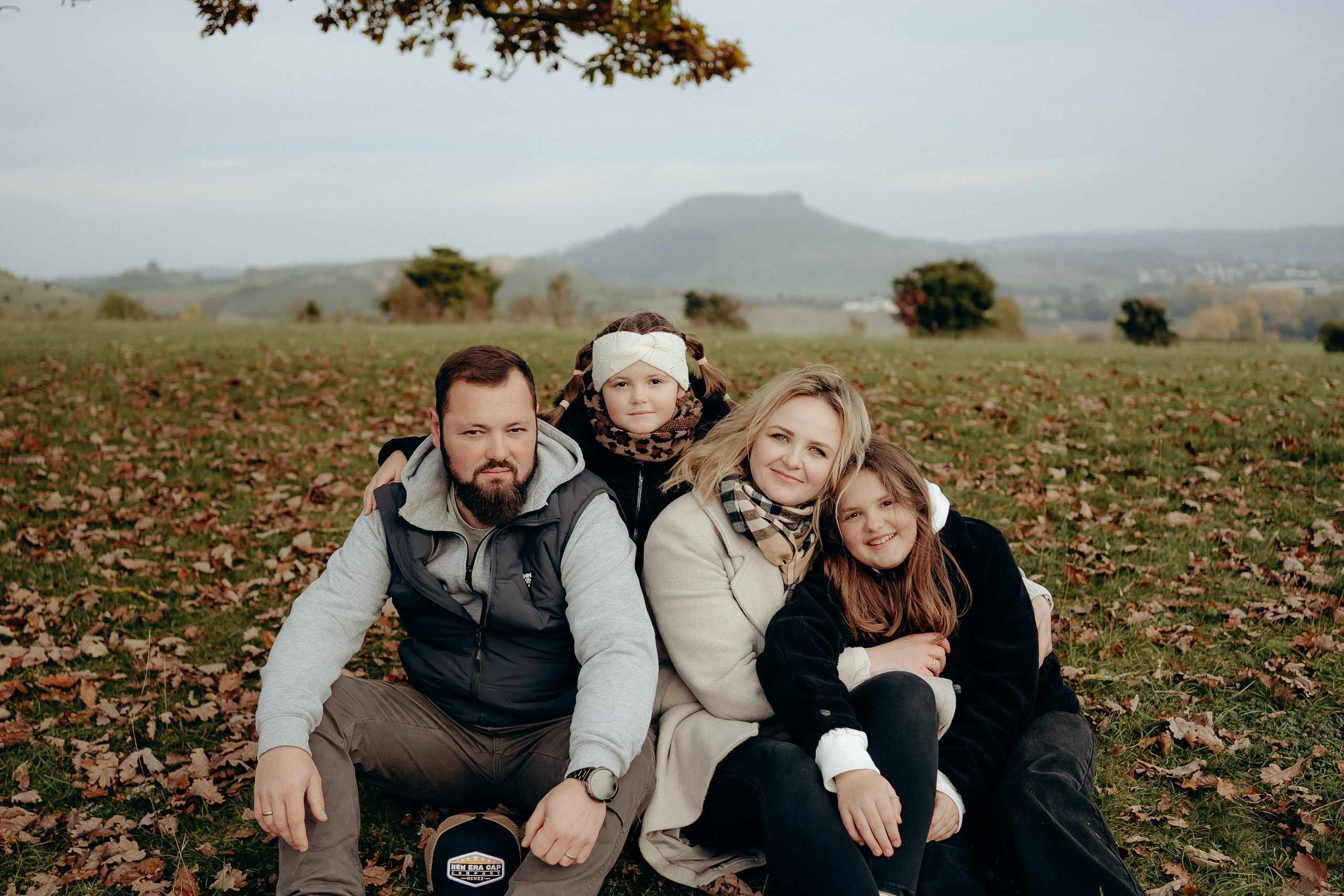 Natürliches Gruppenportrait mehrerer Familienmitglieder, die eng beieinander auf einer Wiese sitzen.