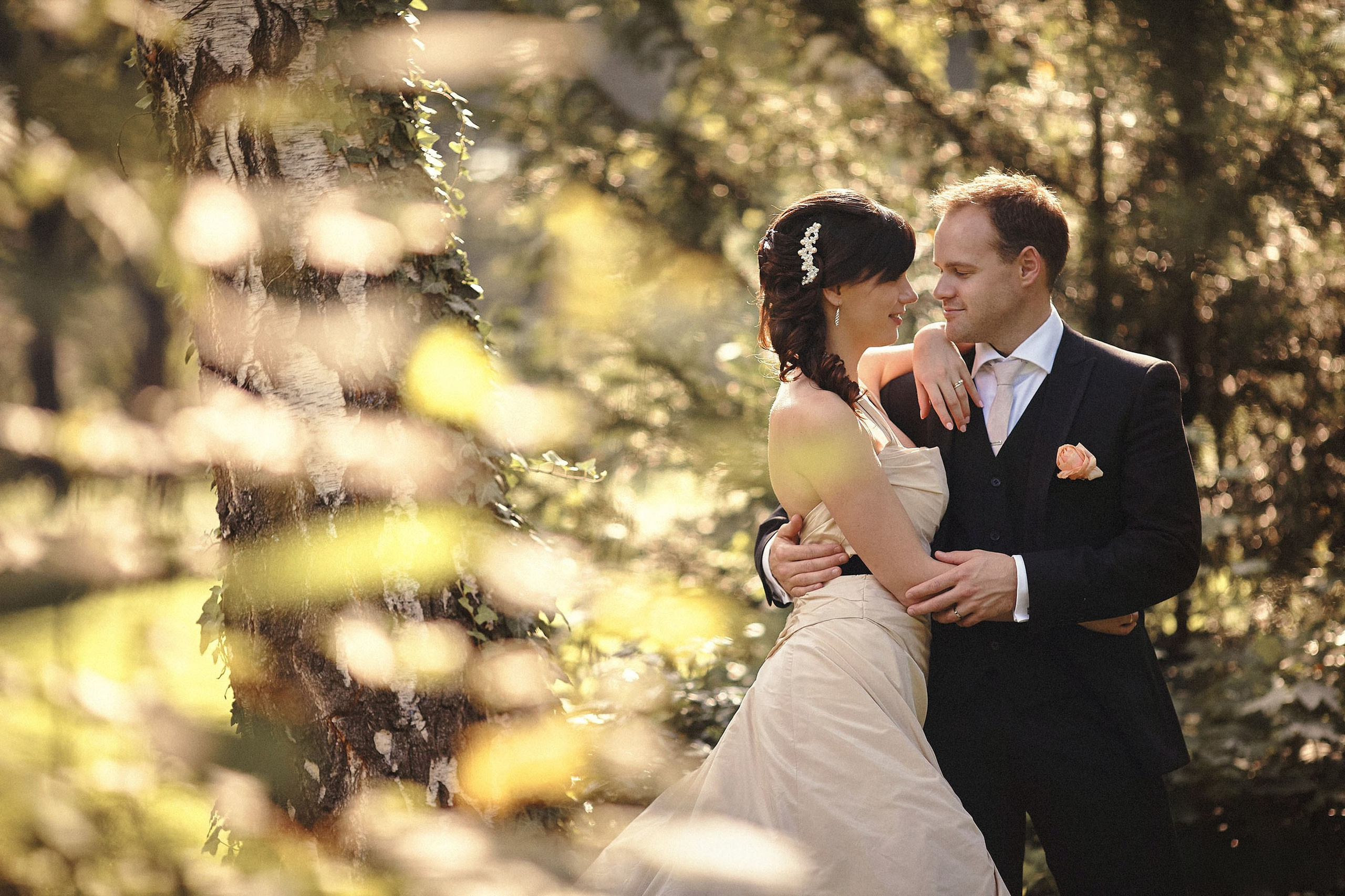 Australian groom embracing Russian bride in sunlit maple forest on their wedding day.