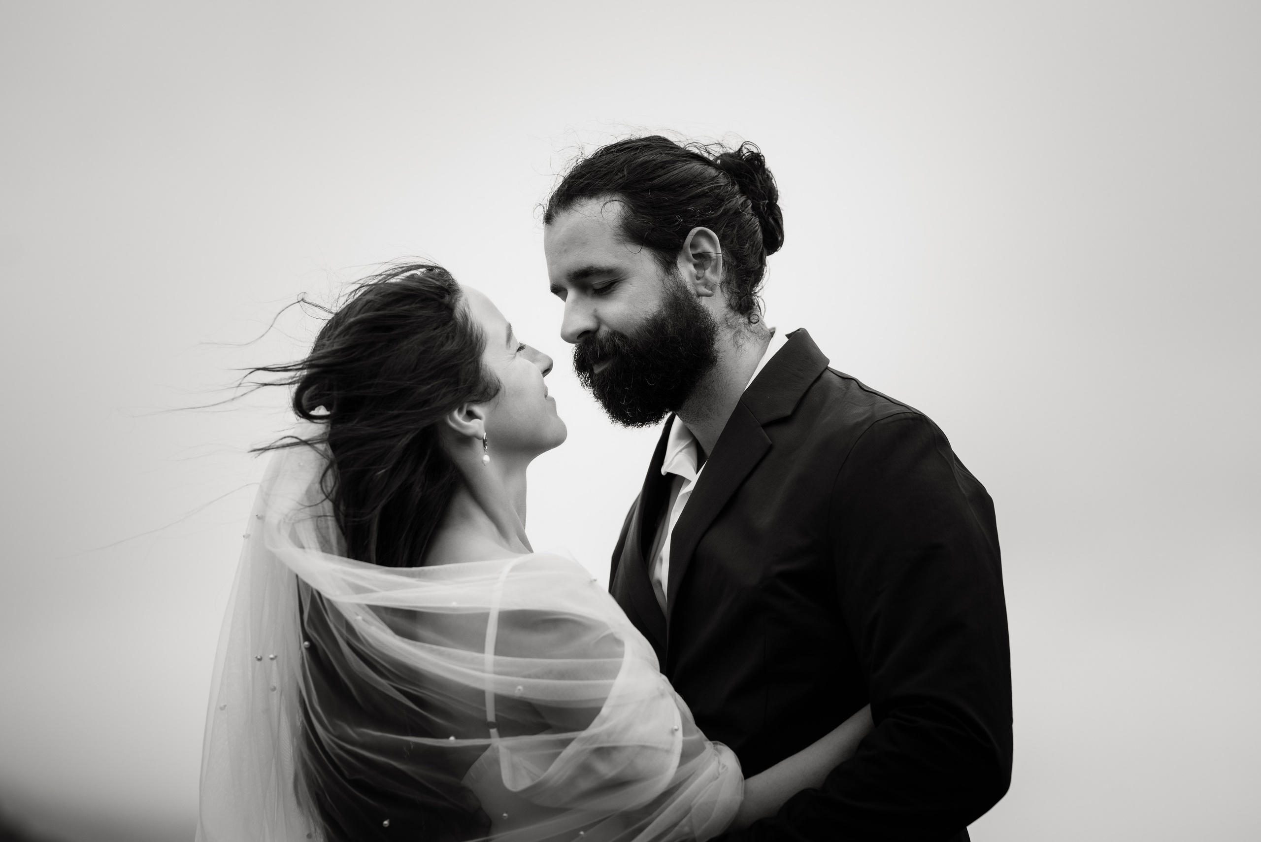 Groom wrapping his arms around the bride as they stand on the rocky edge of Kleifarvatn, braving the cold Icelandic wind.
