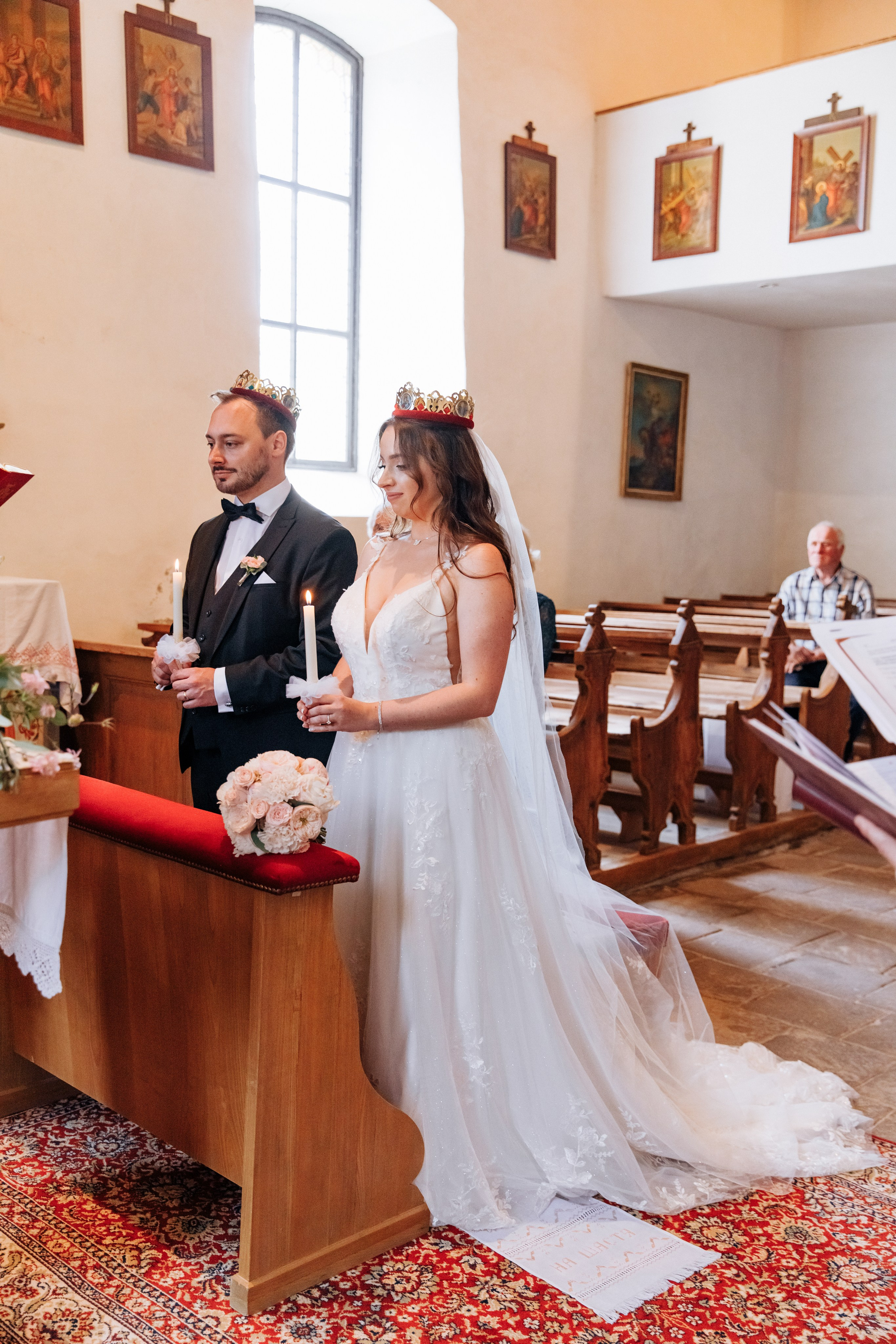 Der Bräutigam und die Braut stehen mit Kerzen in den Händen und tragen goldene Kronen während der Hochzeitszeremonie.