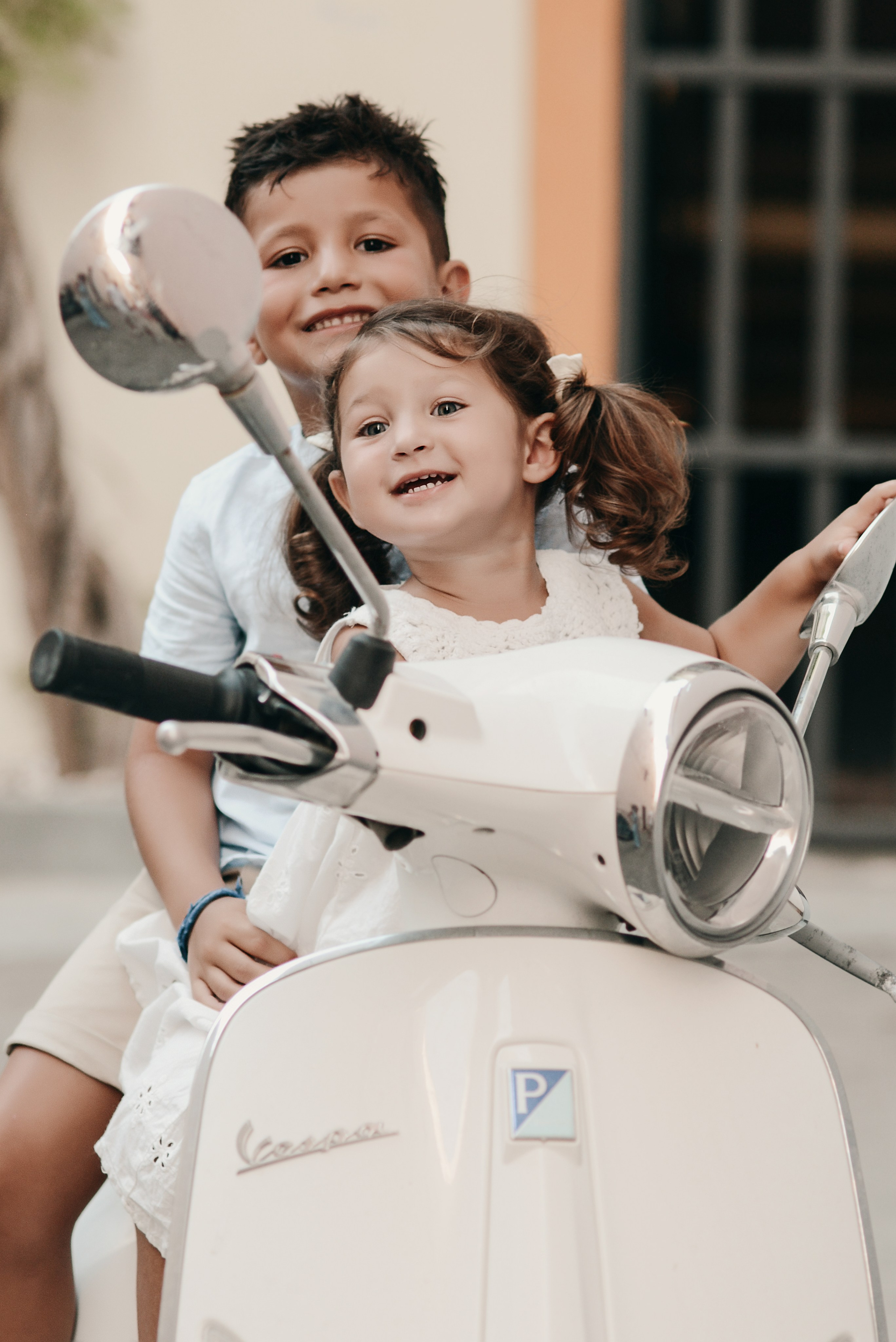 Smiling children posing on a vintage Vespa scooter during a playful photoshoot in southern Italy