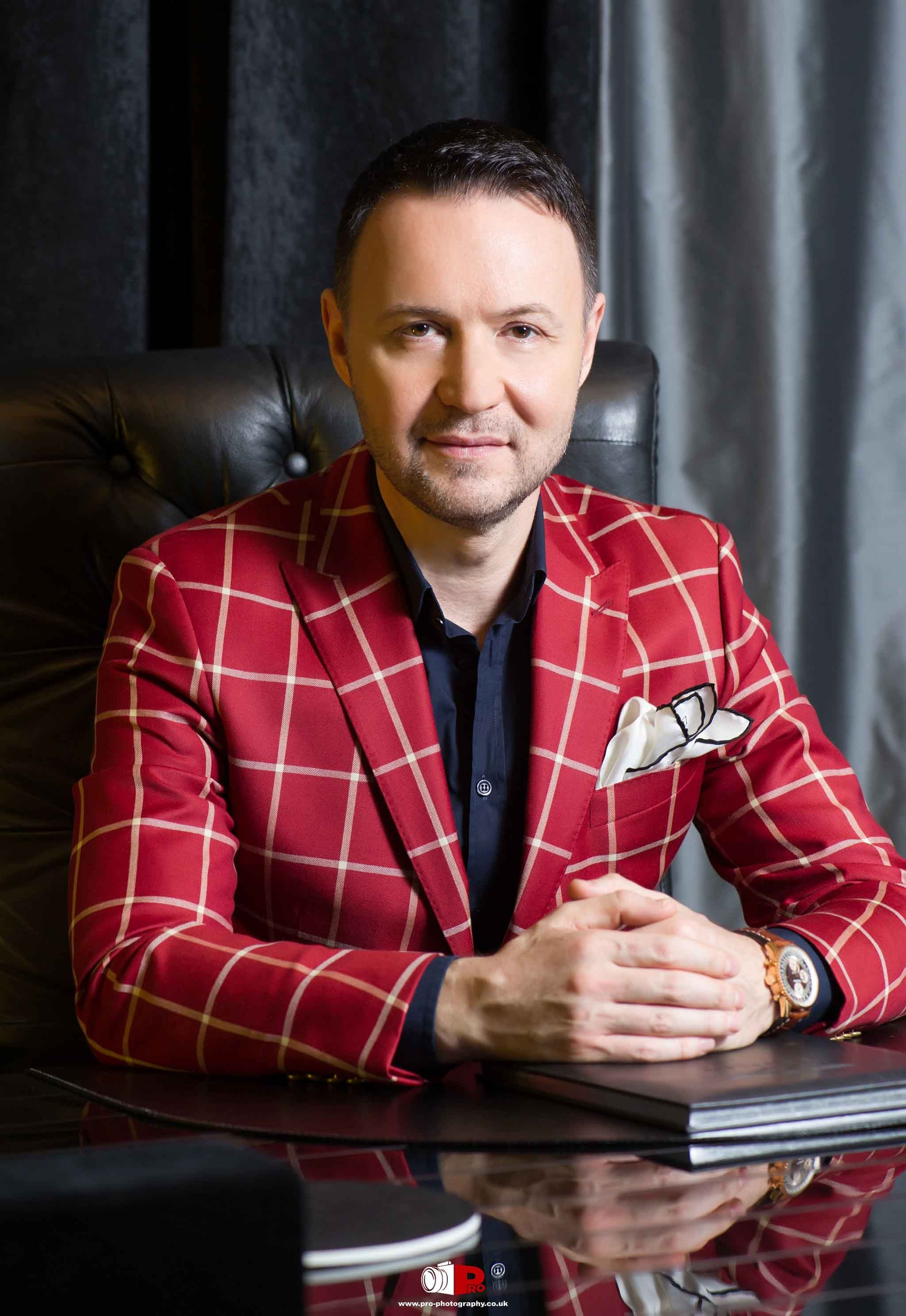 A stylish businessman in a red checkered suit sitting at a desk, exuding confidence and professionalism.