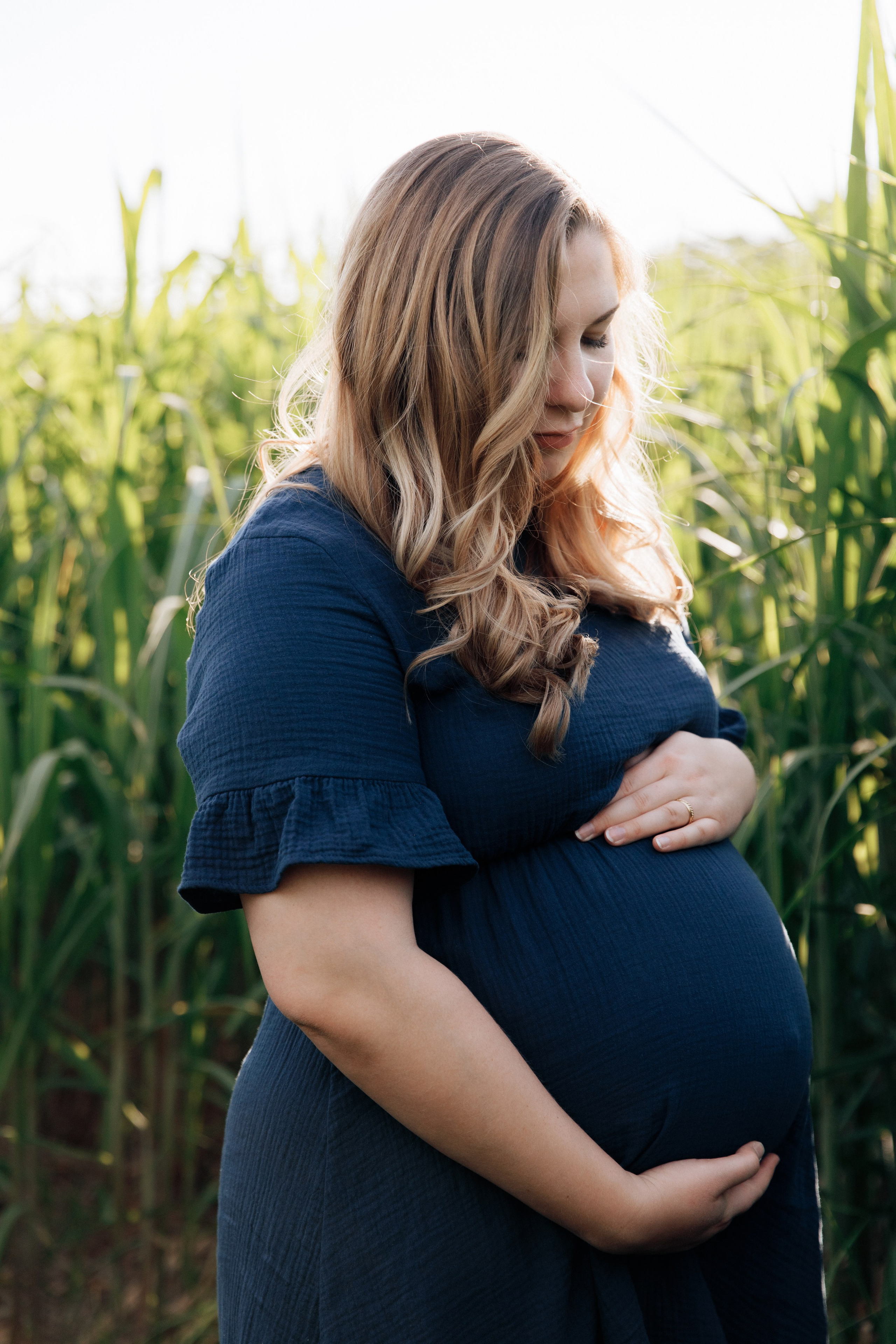 Schwangere Frau steht auf einem Feld und schaut liebevoll auf ihren Babybauch.