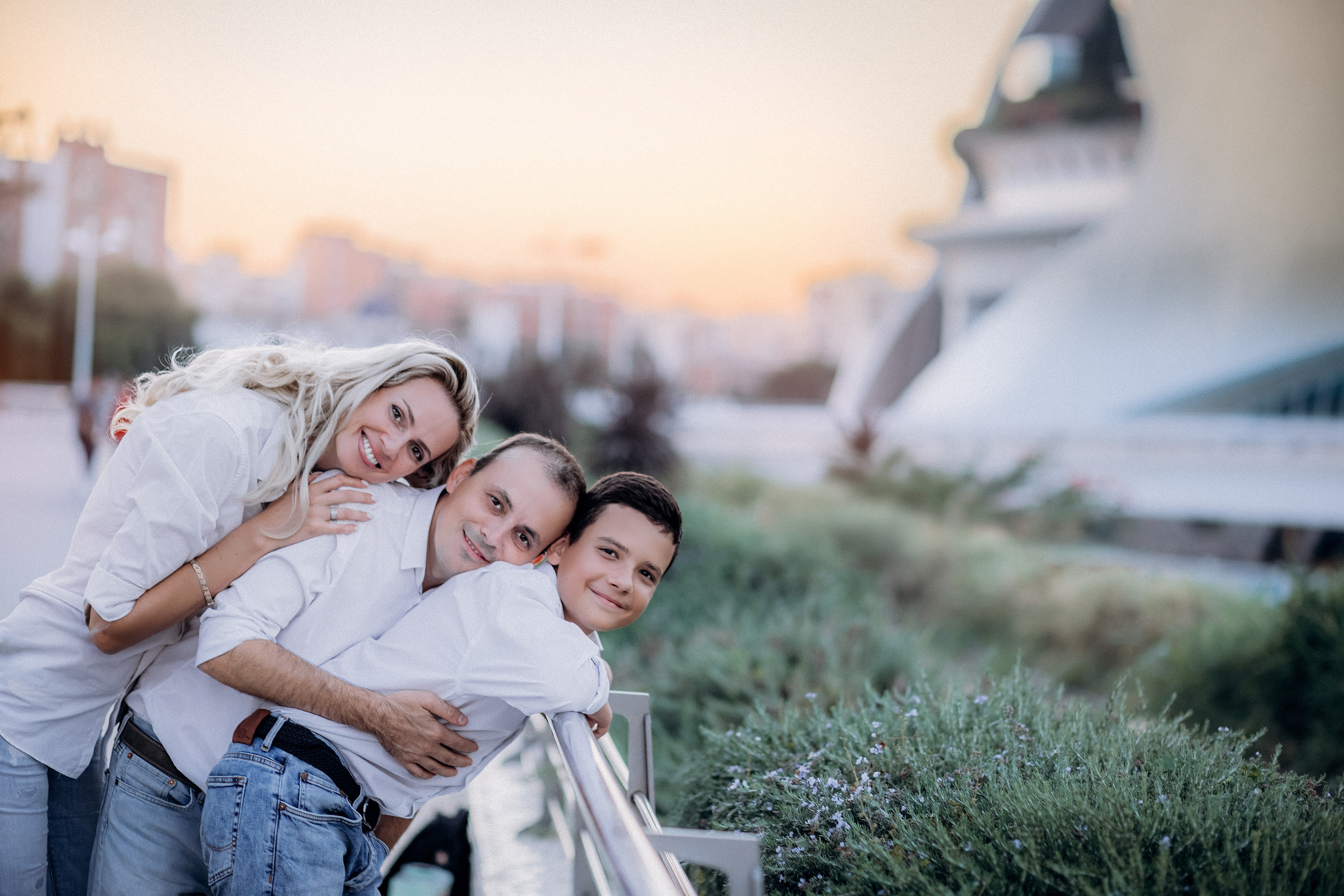 Familia sonriente apoyada en una barandilla junto a la Ciudad de las Artes y las Ciencias durante una sesión familiar al atardecer en Valencia, España — un momento alegre y espontáneo perfecto para quienes buscan fotografía familiar natural y conmovedora en Valencia y toda España.