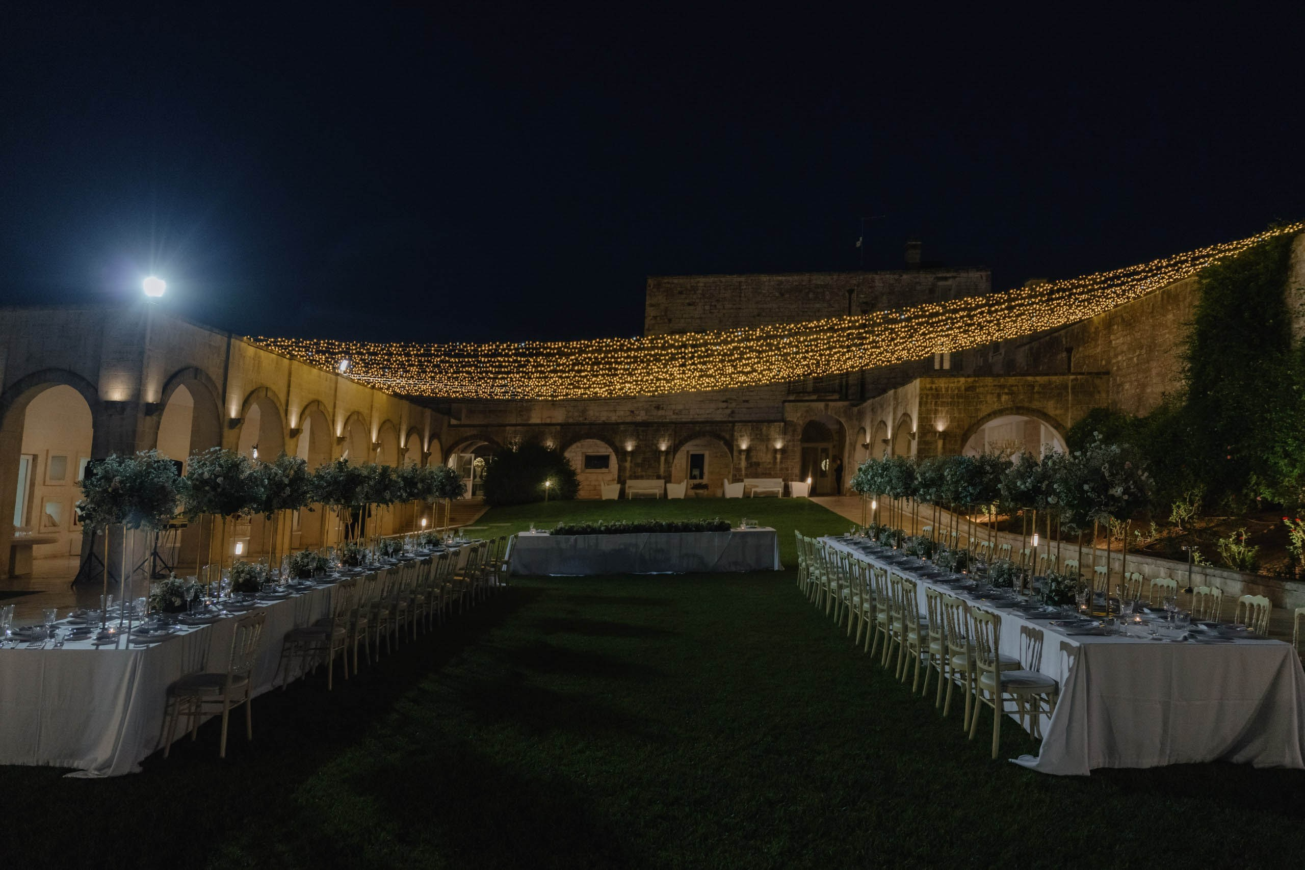 Outdoor wedding dinner setup with long tables and soft lighting, luxury destination wedding in Puglia Italy
