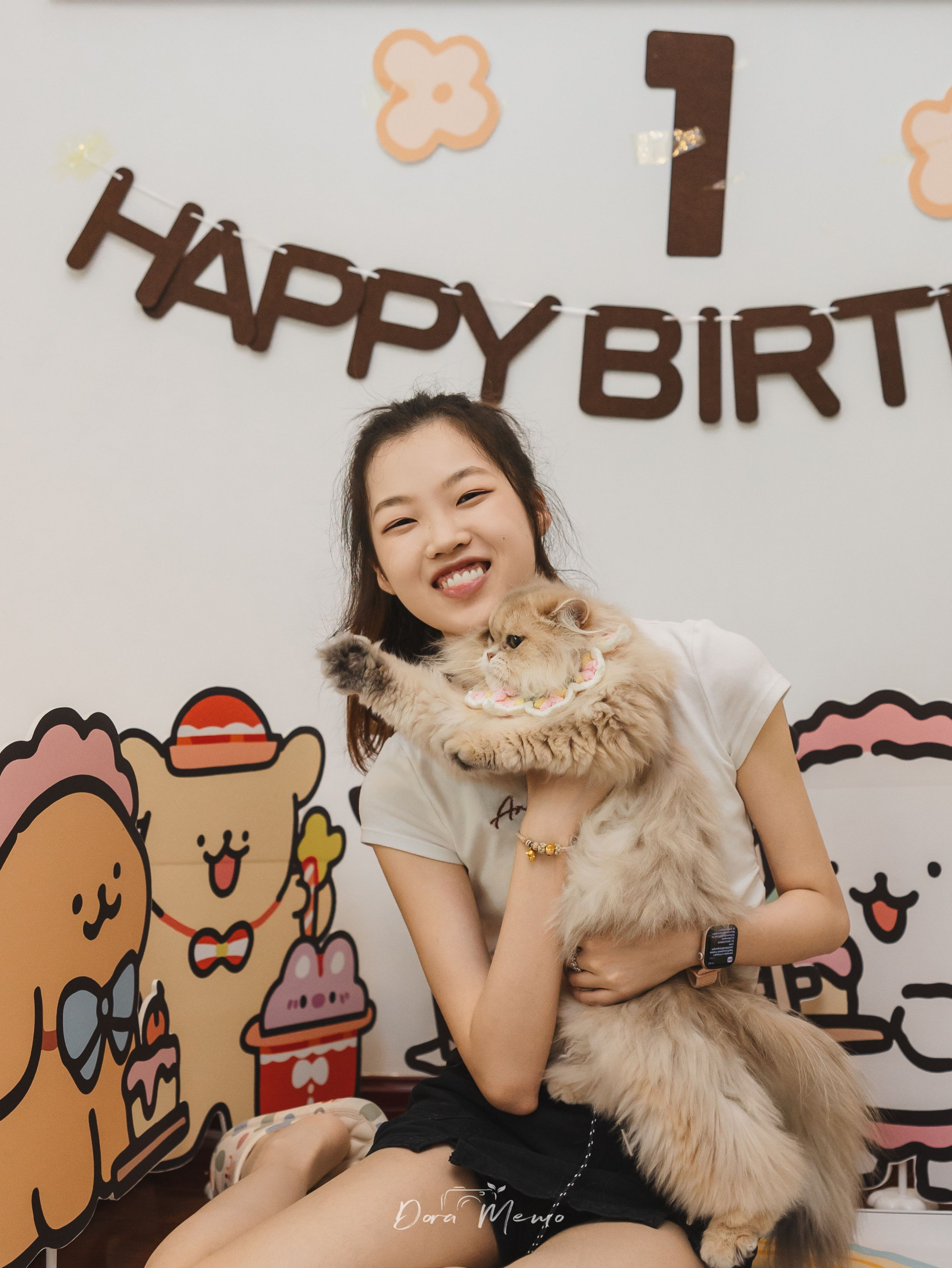  A woman holding her cat in front of a first birthday backdrop during an at-home pet family photography session in Shanghai.