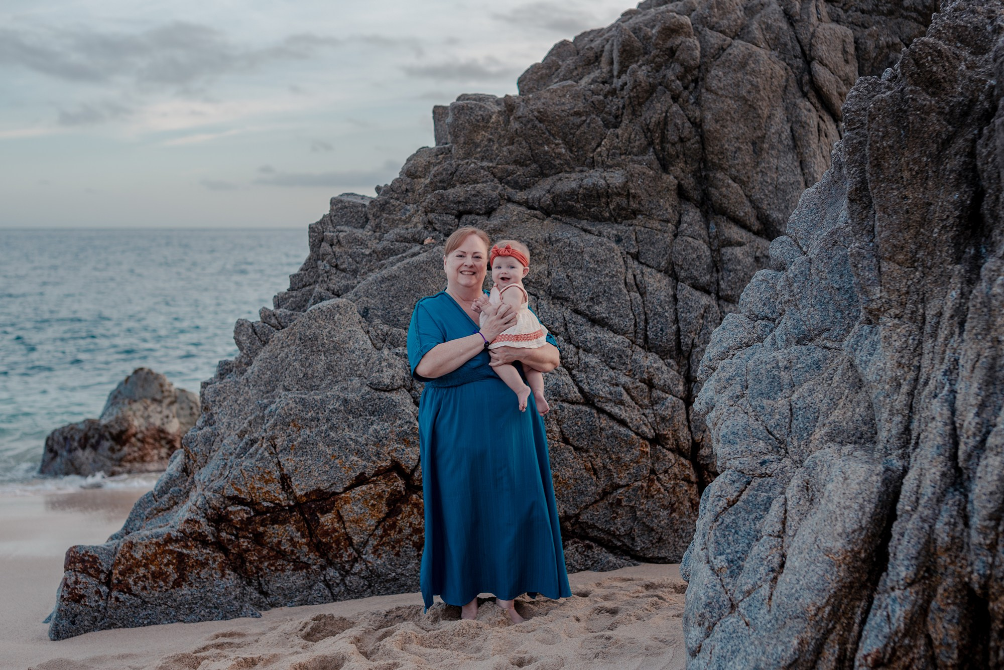 Grandmother holding grandchild during multi-generational family beach session at Playa Monumentos Cabo San Lucas Mexico
