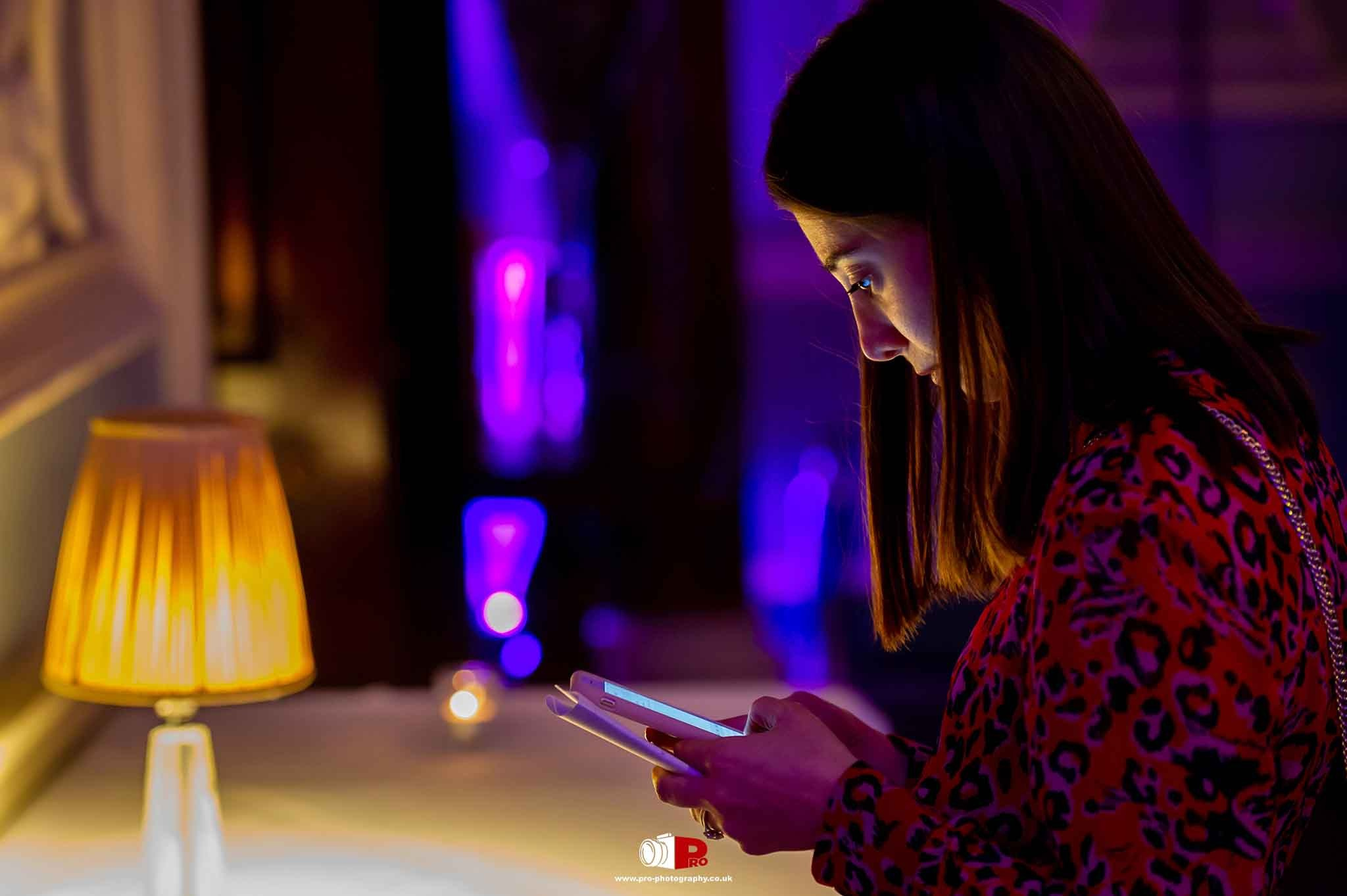 A woman in a red leopard print dress engrossed in her smartphone, illuminated by vibrant purple lighting.