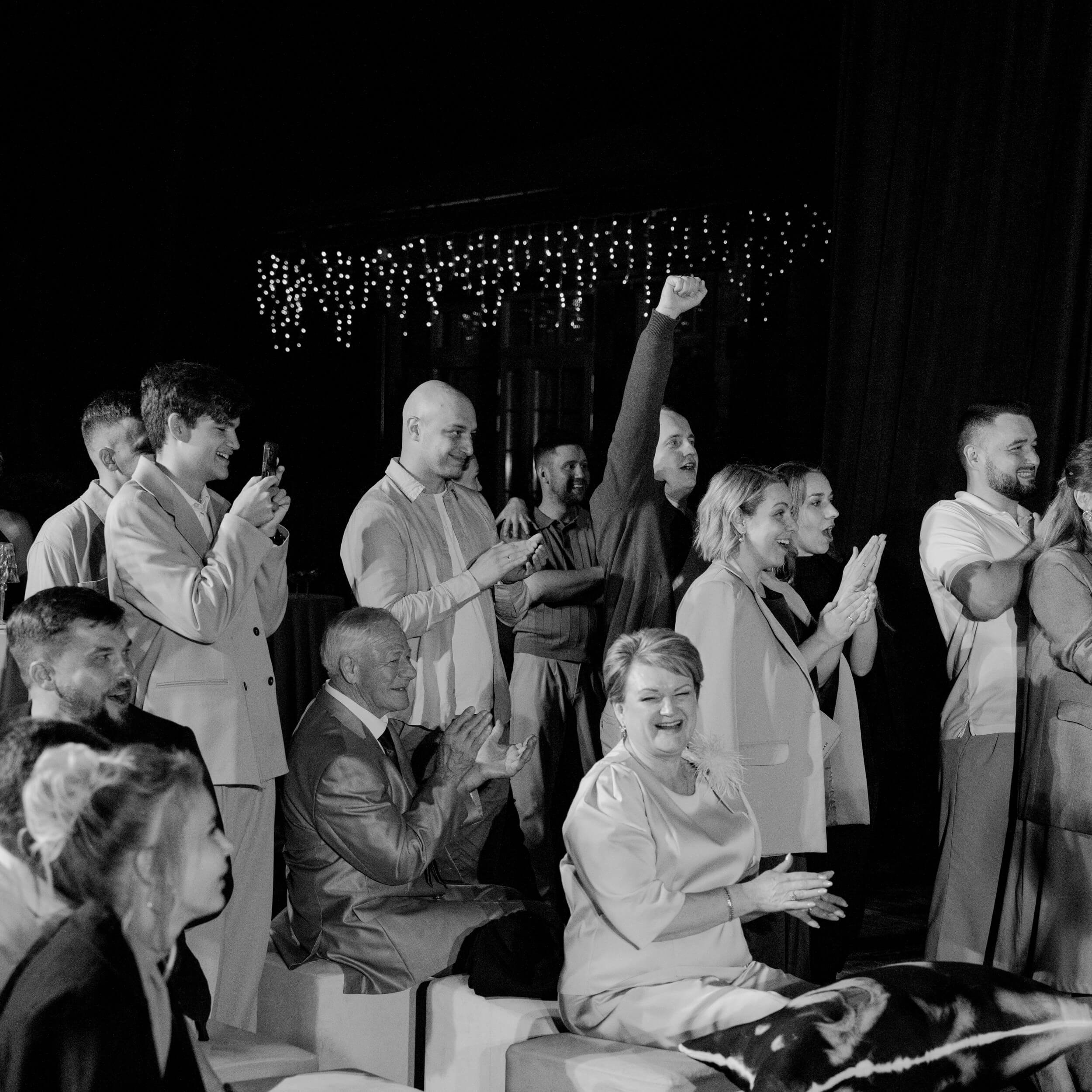 Black and white wide shot of a large crowd of wedding guests celebrating on the dance floor with hands raised, energetic party at Lake Como wedding ceremony