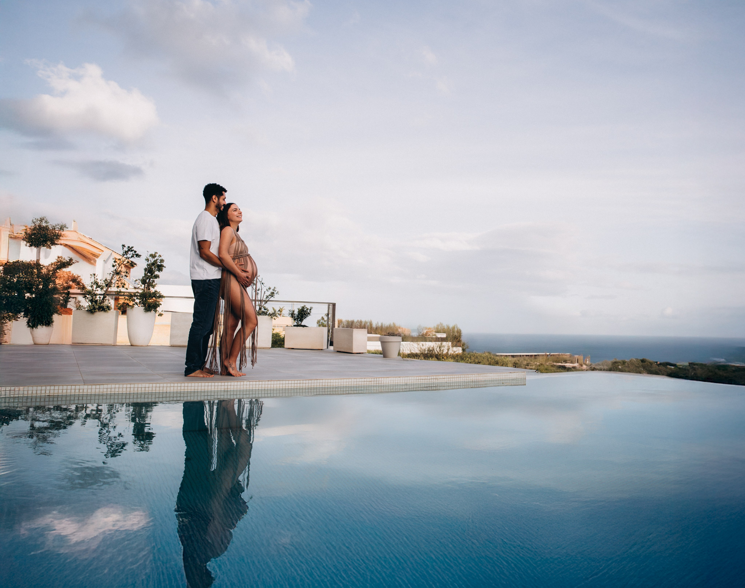 Elegante sesión de embarazo junto a una piscina privada en Málaga, España — una pareja celebra la belleza del embarazo bajo un cielo sereno y un entorno elegante. Ideal para quienes buscan sesiones de fotos de embarazo al aire libre y con estilo en Málaga y el sur de España.