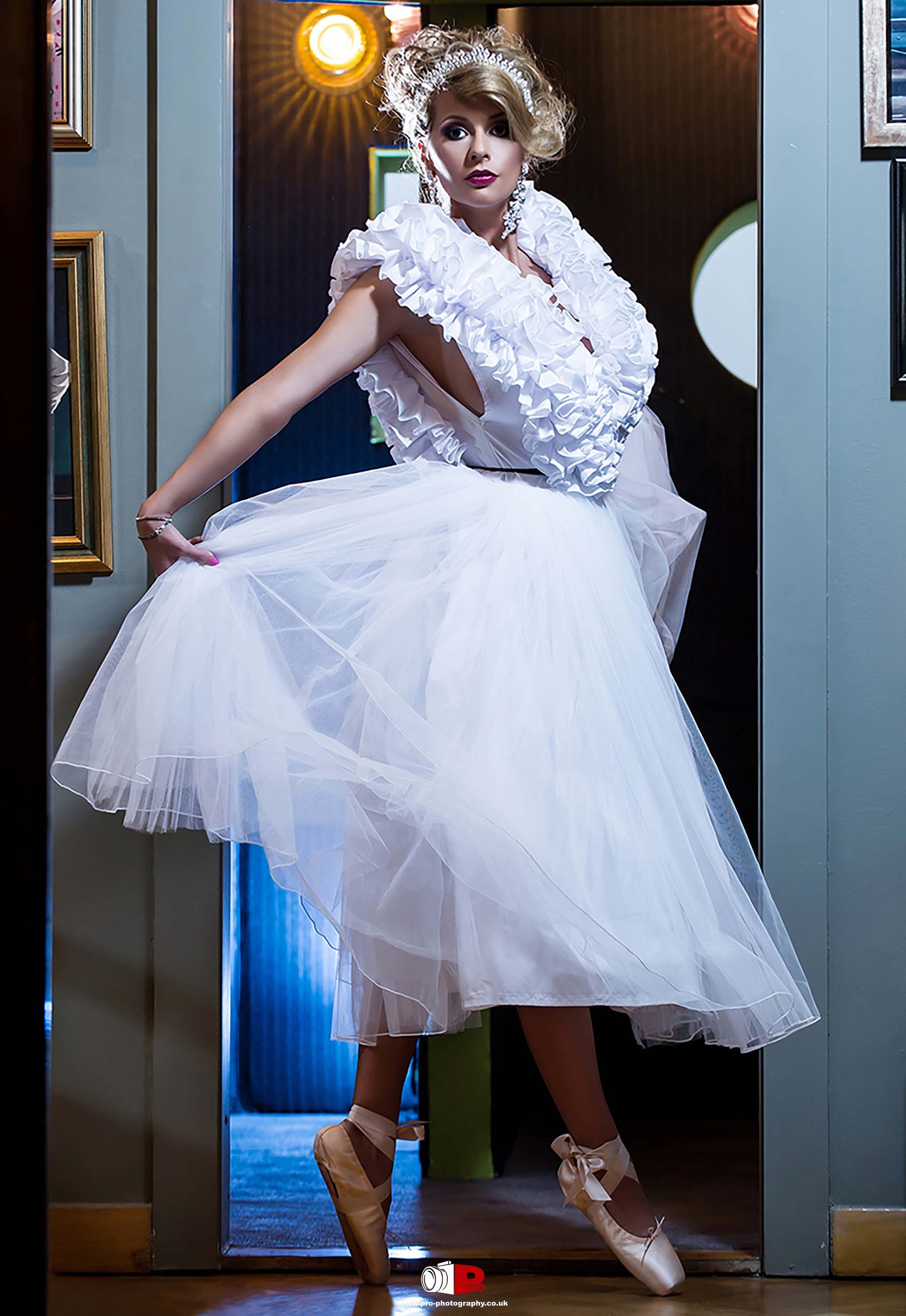  A poised ballerina in a white ruffled gown and tiara performing a graceful pose.