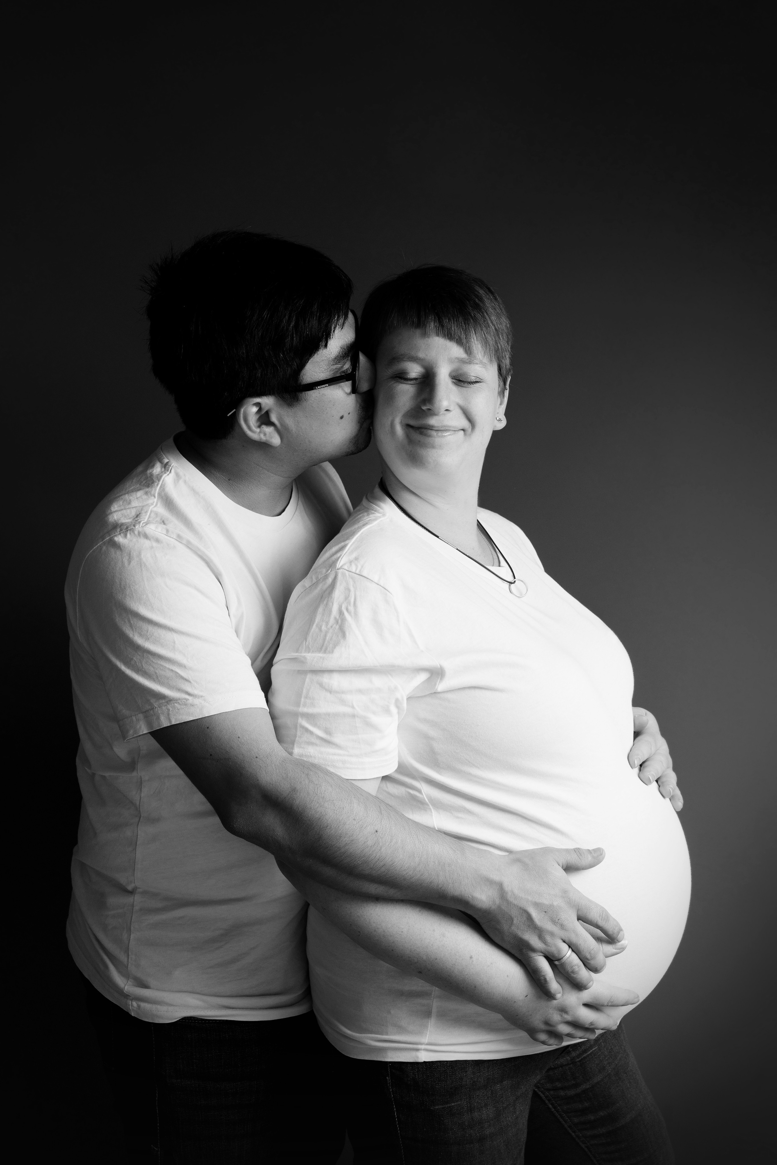 Ein Mann hält stolz seine schwangere Frau und küsst sie auf die Stirn